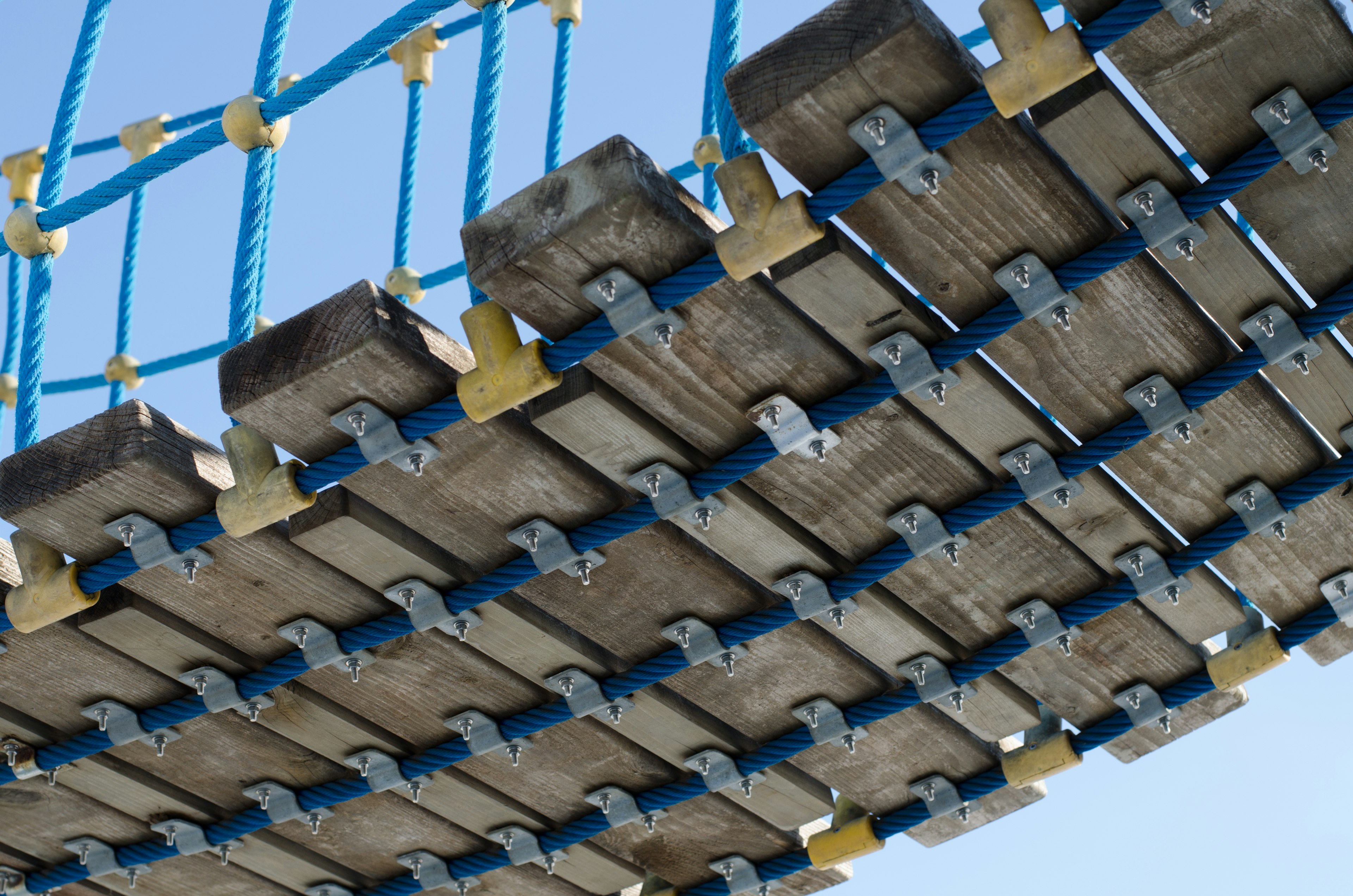 Underside structure of a wooden suspension bridge supported by blue ropes