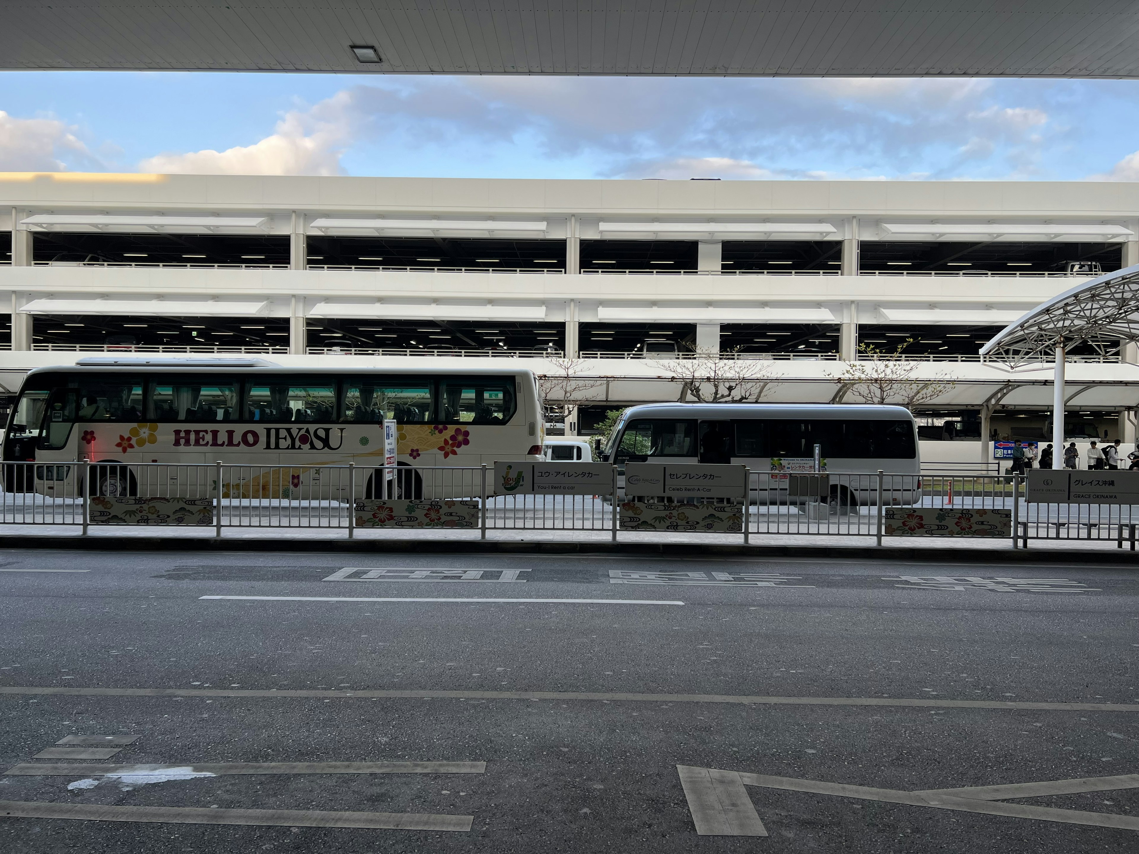 Buses parked at an airport bus stop with a parking structure in the background