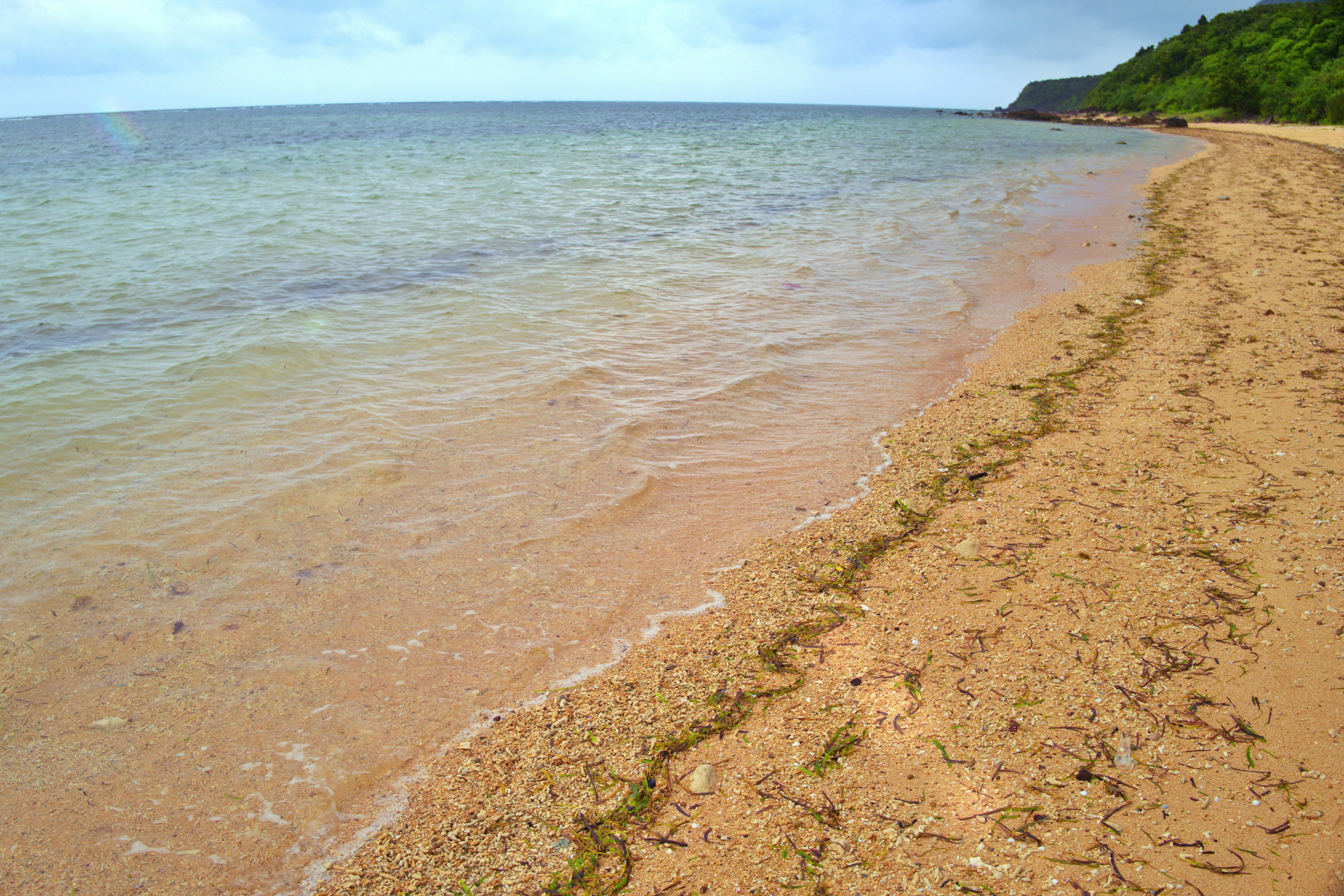 ฉากชายหาดสงบพร้อมคลื่นอ่อน ชายหาดทราย เนินเขาสีเขียวและท้องฟ้าสีฟ้า