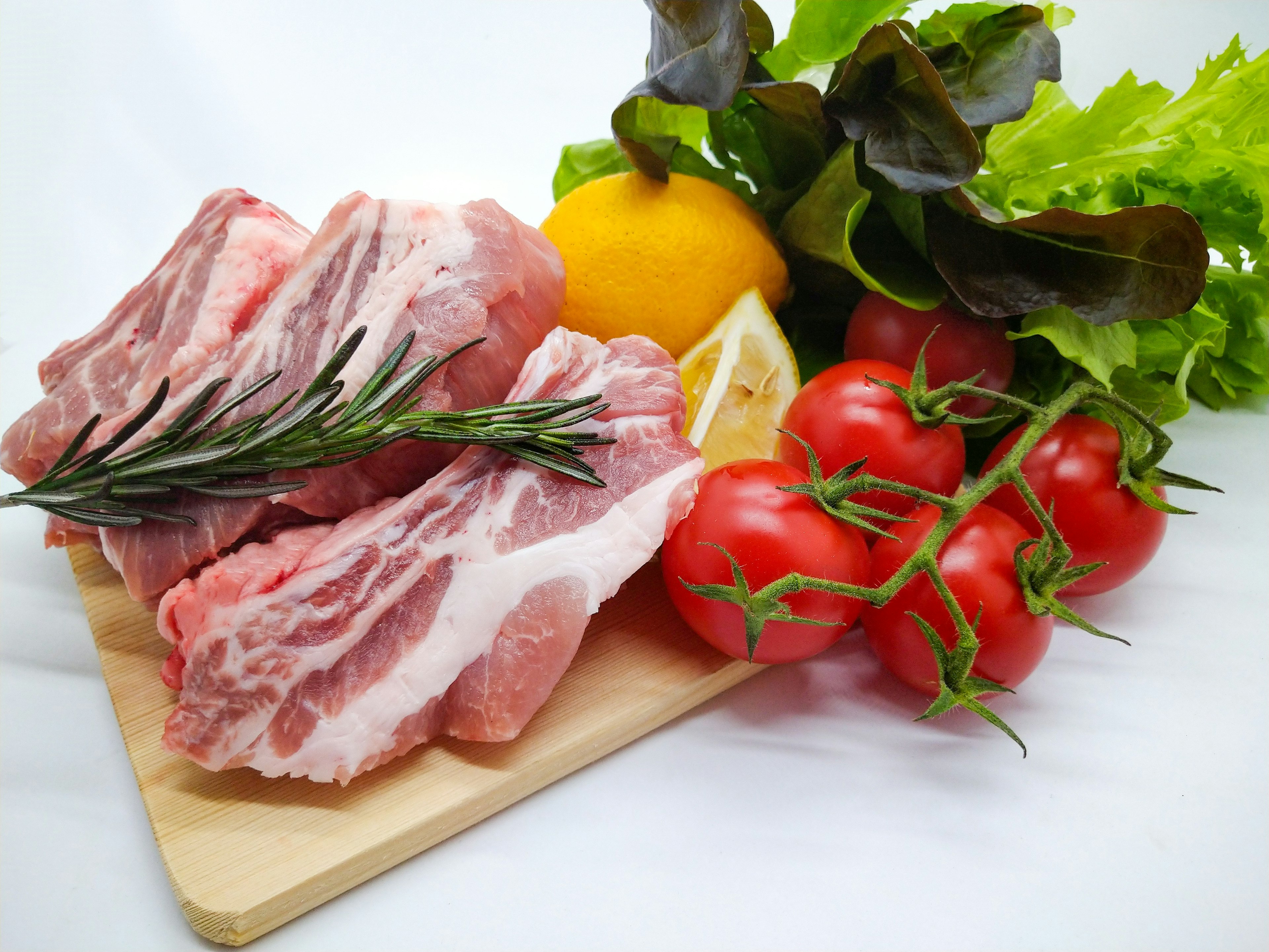 Fette di carne fresca con pomodori limone e verdure disposte su un tagliere di legno