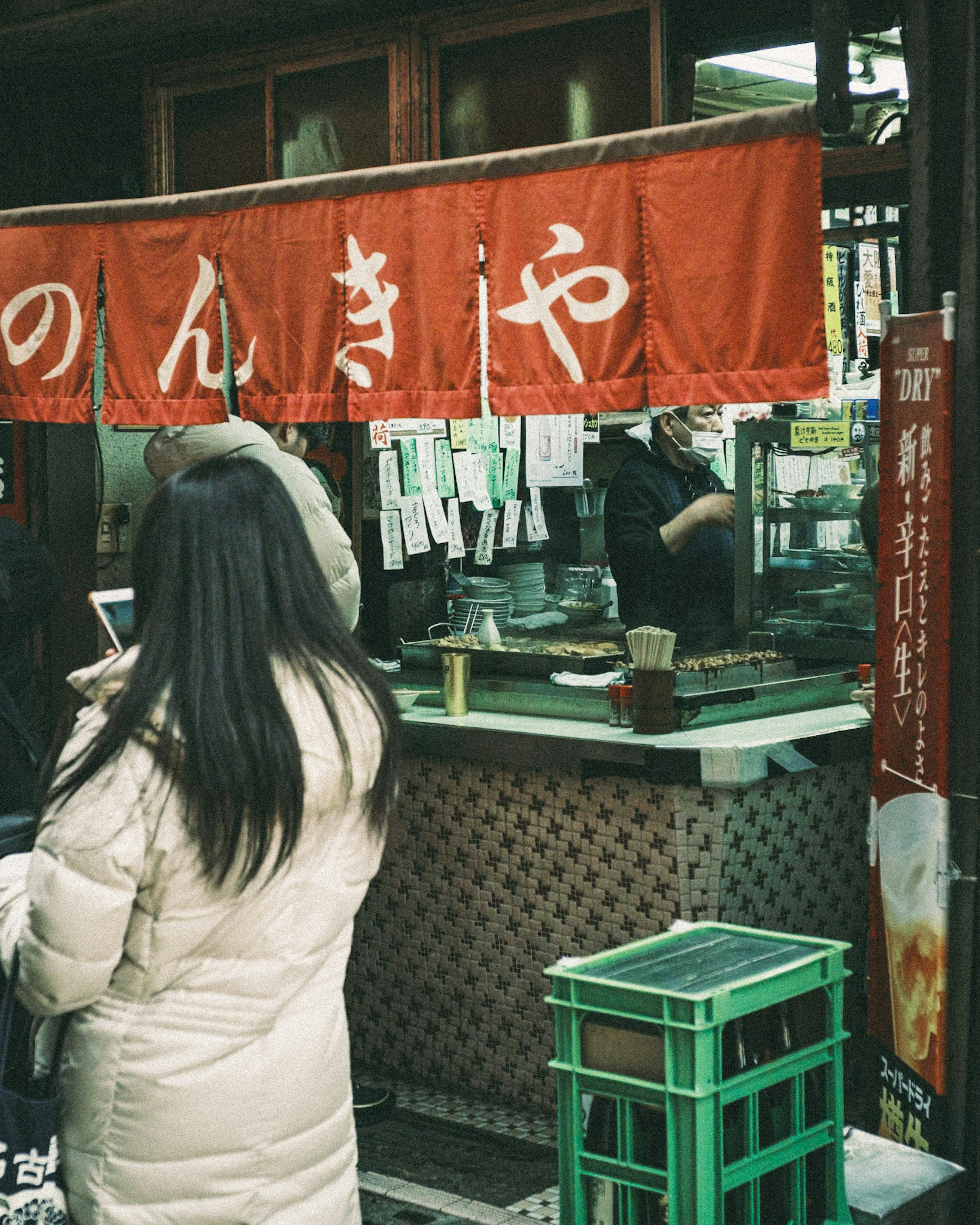 A woman standing in front of a food stall with a red noren curtain