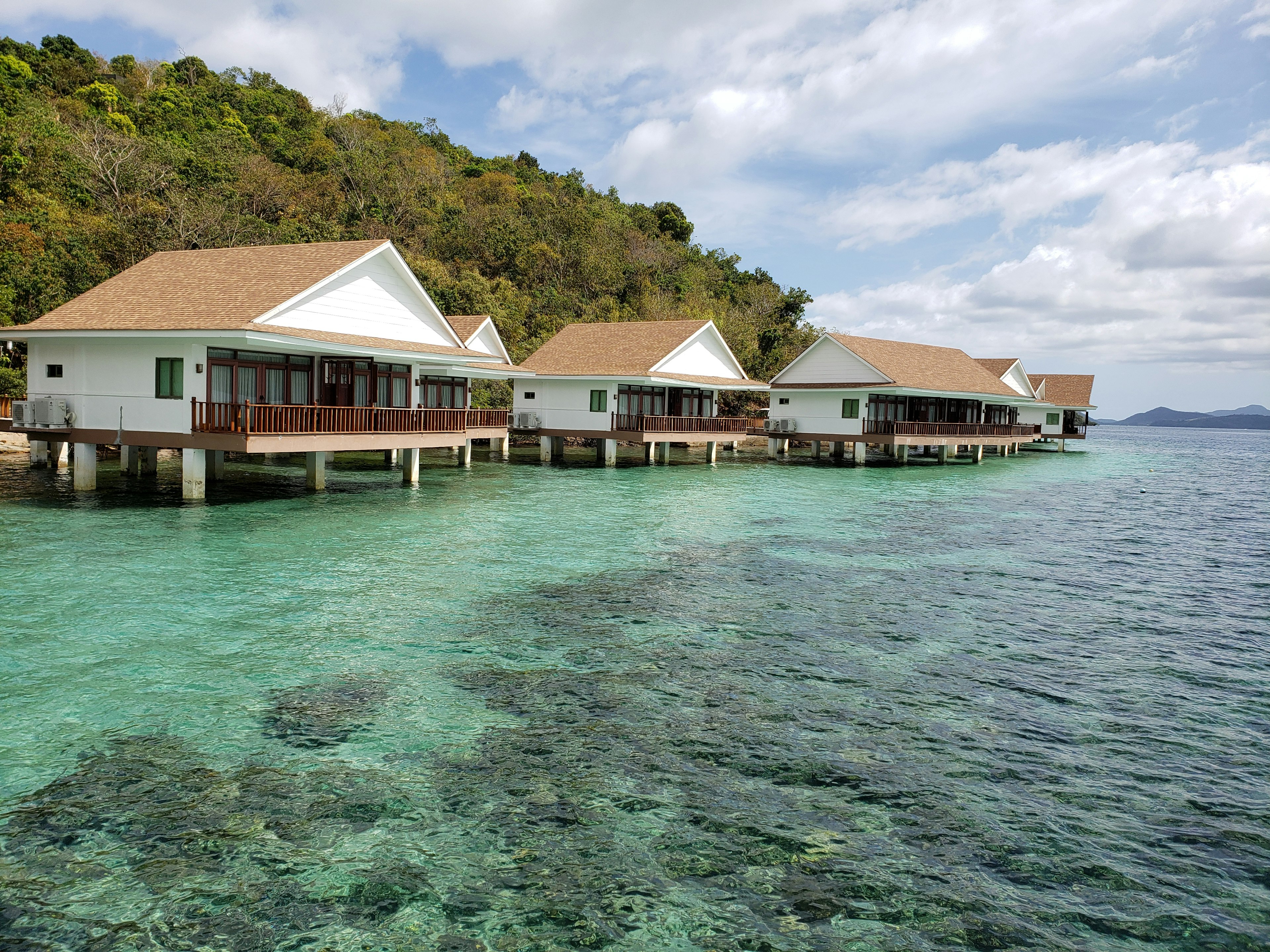 Bungalow di atas air di perairan biru jernih dikelilingi vegetasi