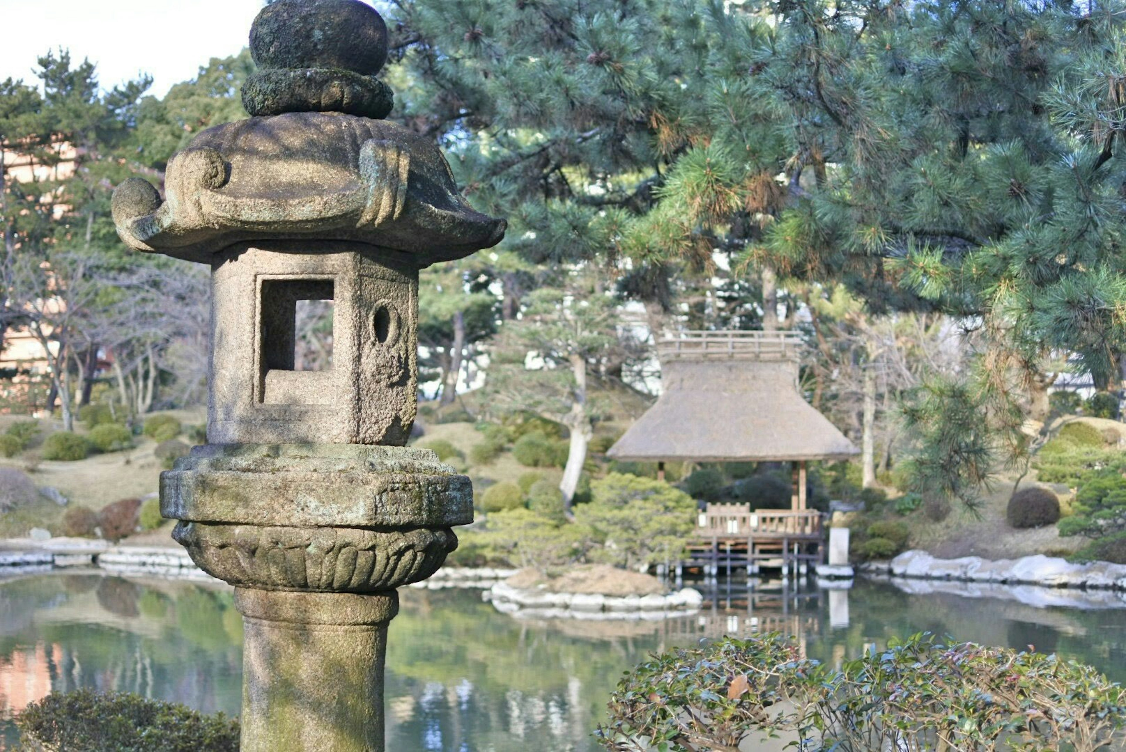 Linterna de piedra en un jardín japonés con estanque y pabellón tradicional