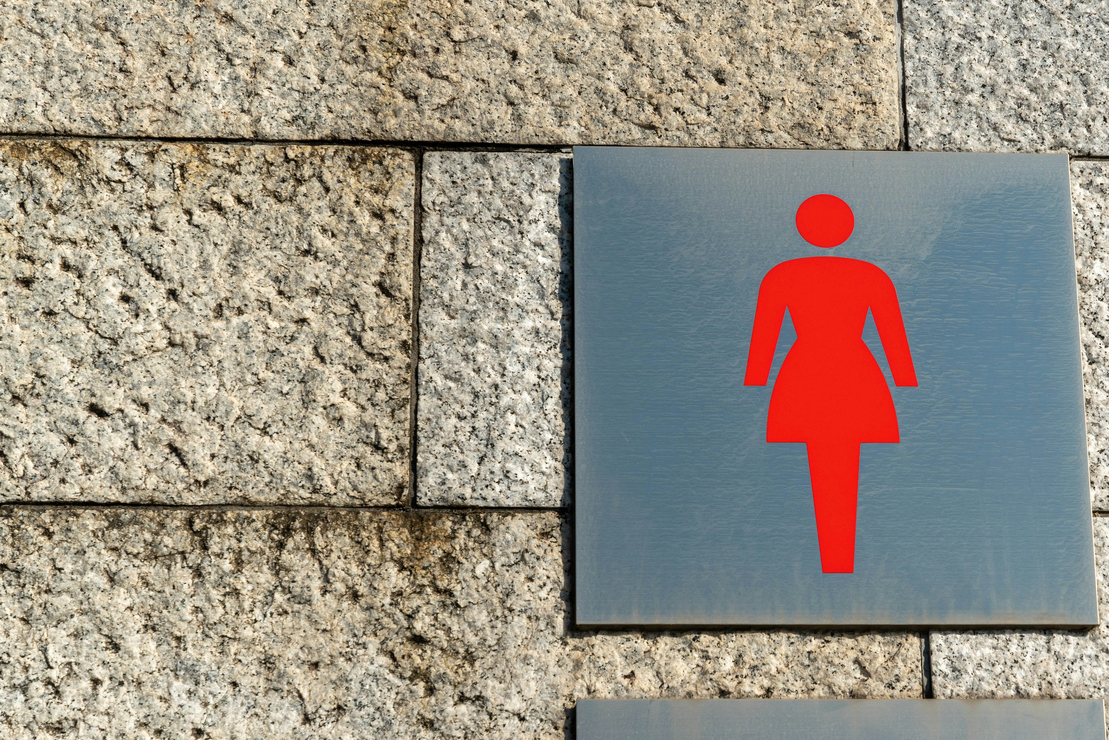 Red women's restroom sign mounted on a stone wall