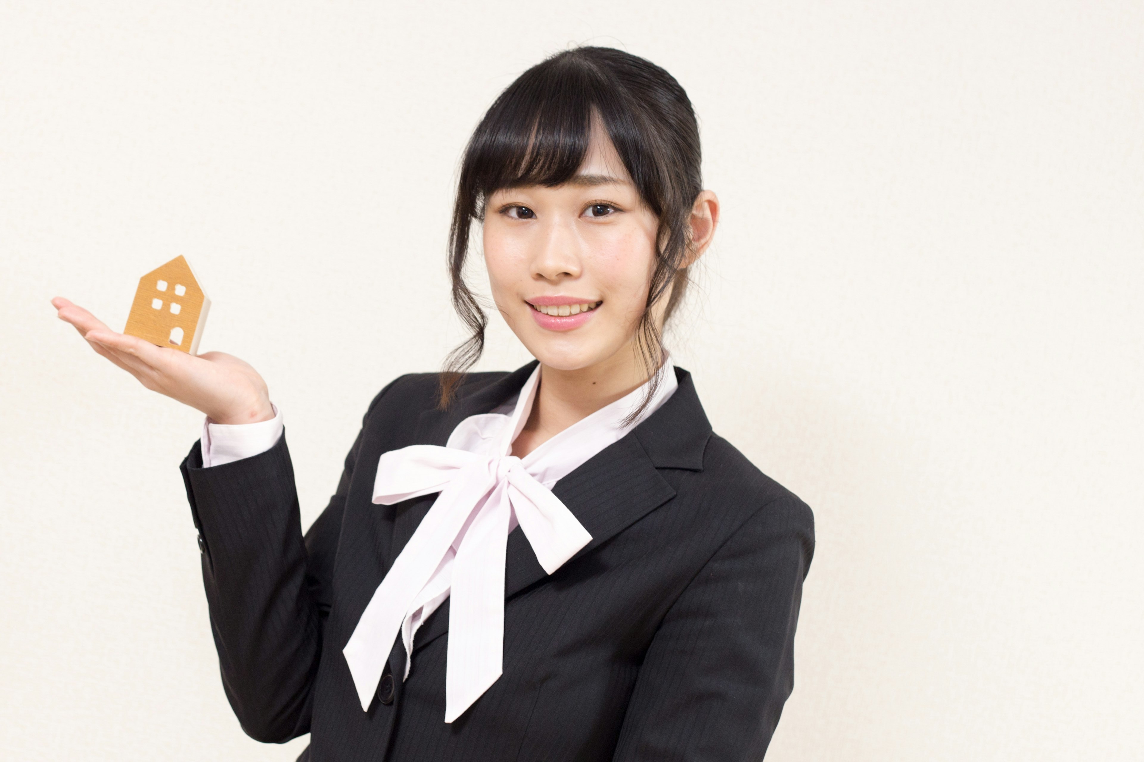 A woman in a suit holding a model house and smiling