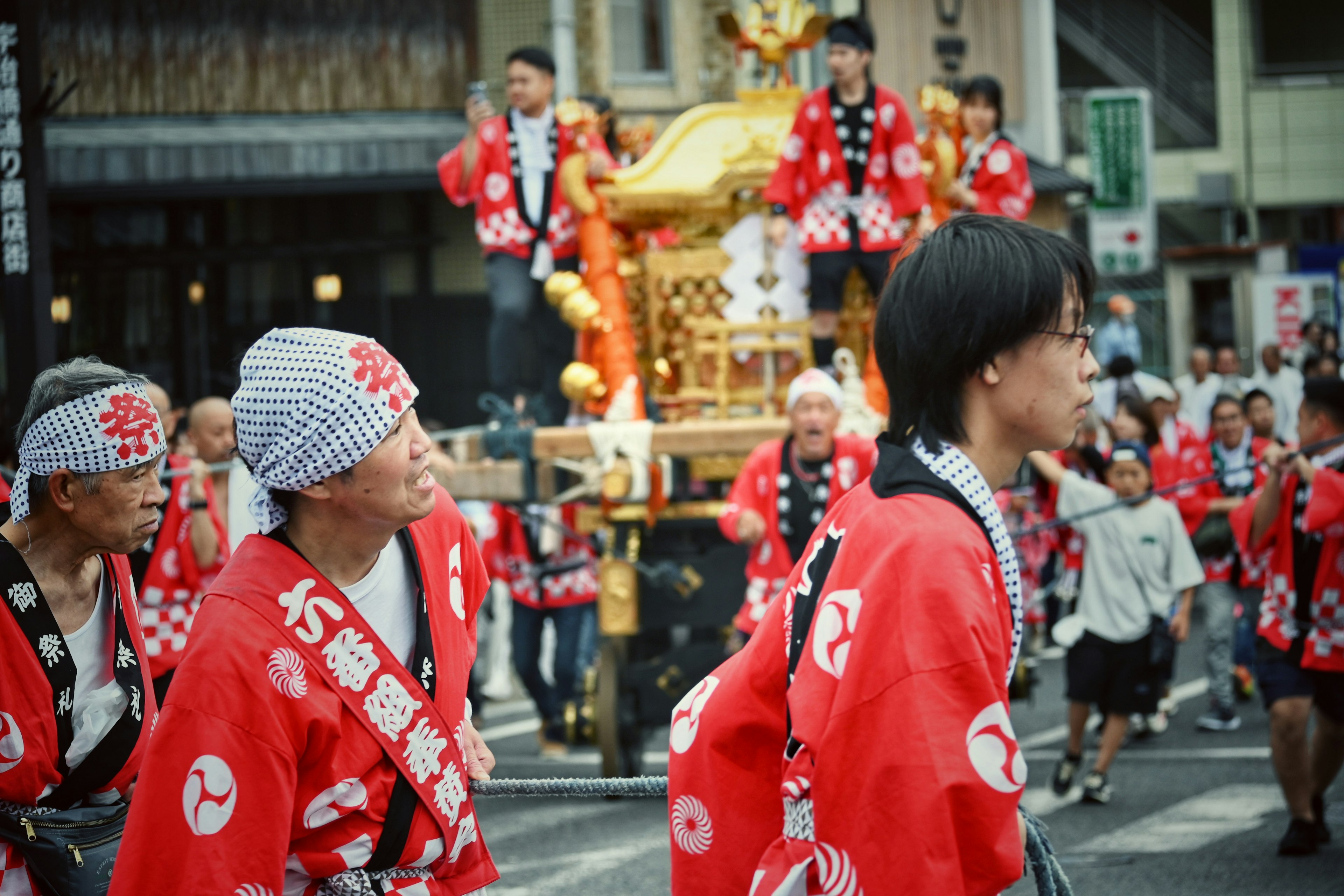 Menschen in Festkleidung marschieren lebendige rote Happi-Jacken und weiße Bandanas traditionelles Mikoshi im Hintergrund