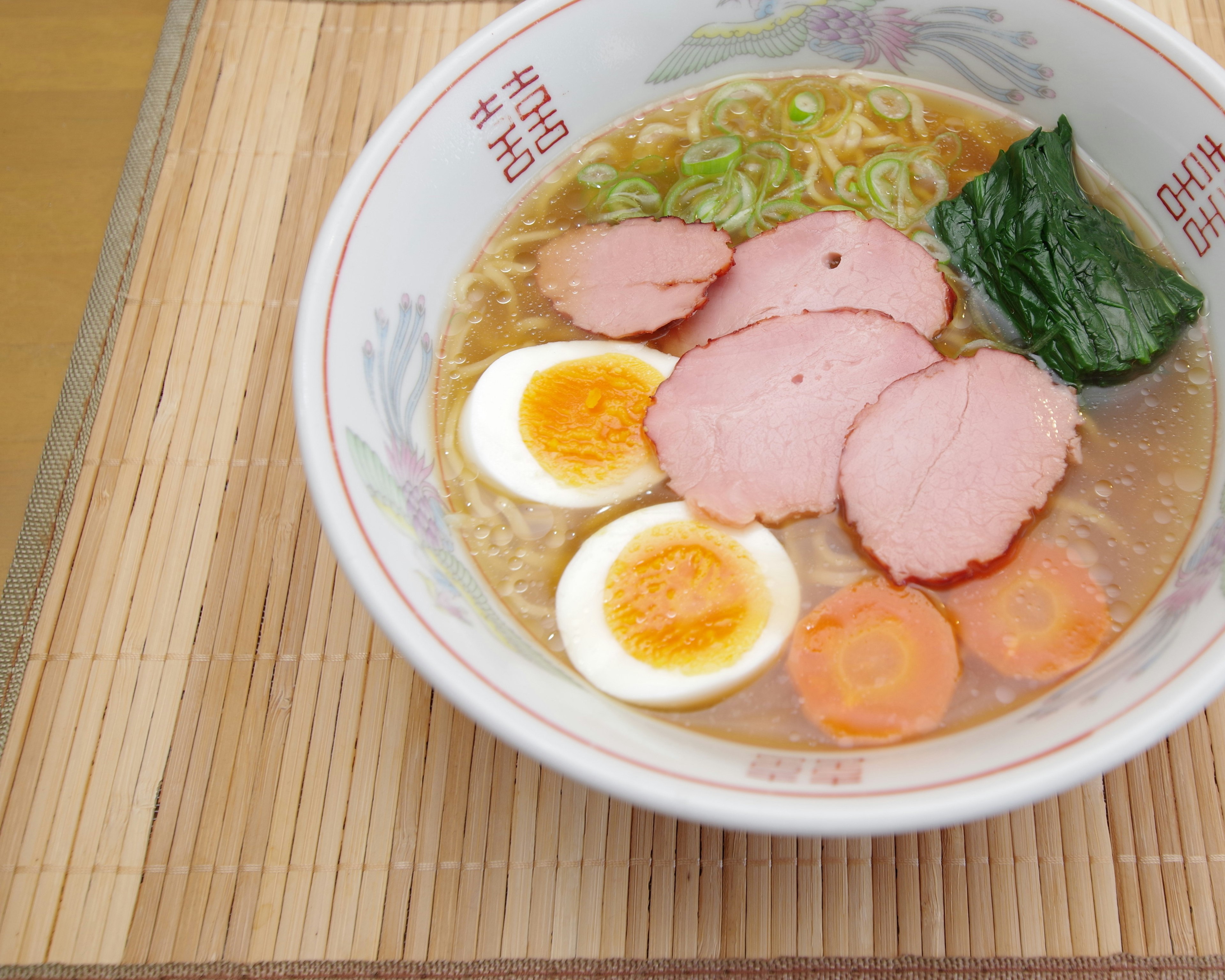 A bowl of ramen featuring sliced chashu, soft boiled eggs, green onions, spinach, and carrots