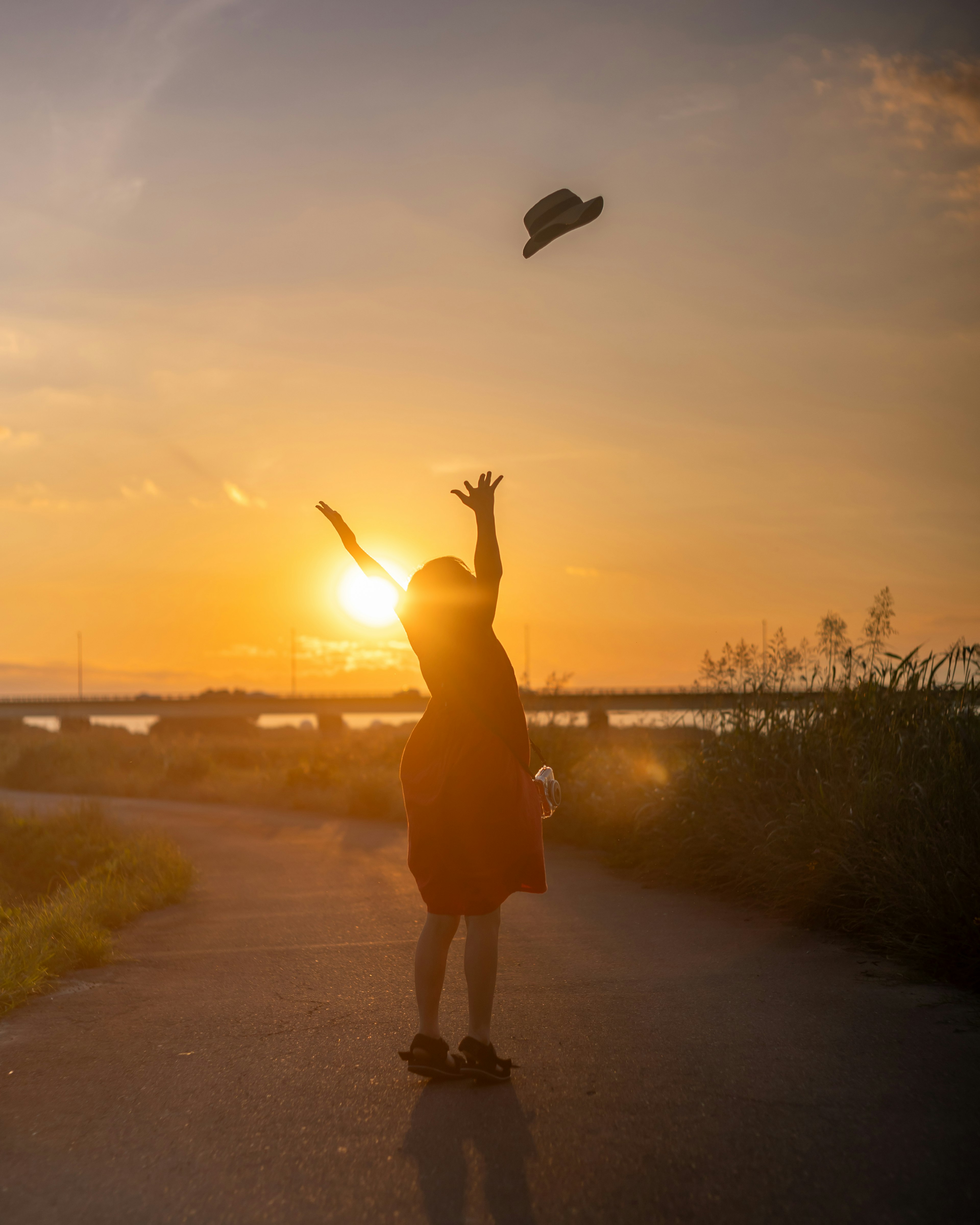 夕日を背景に帽子を投げる女性のシルエット