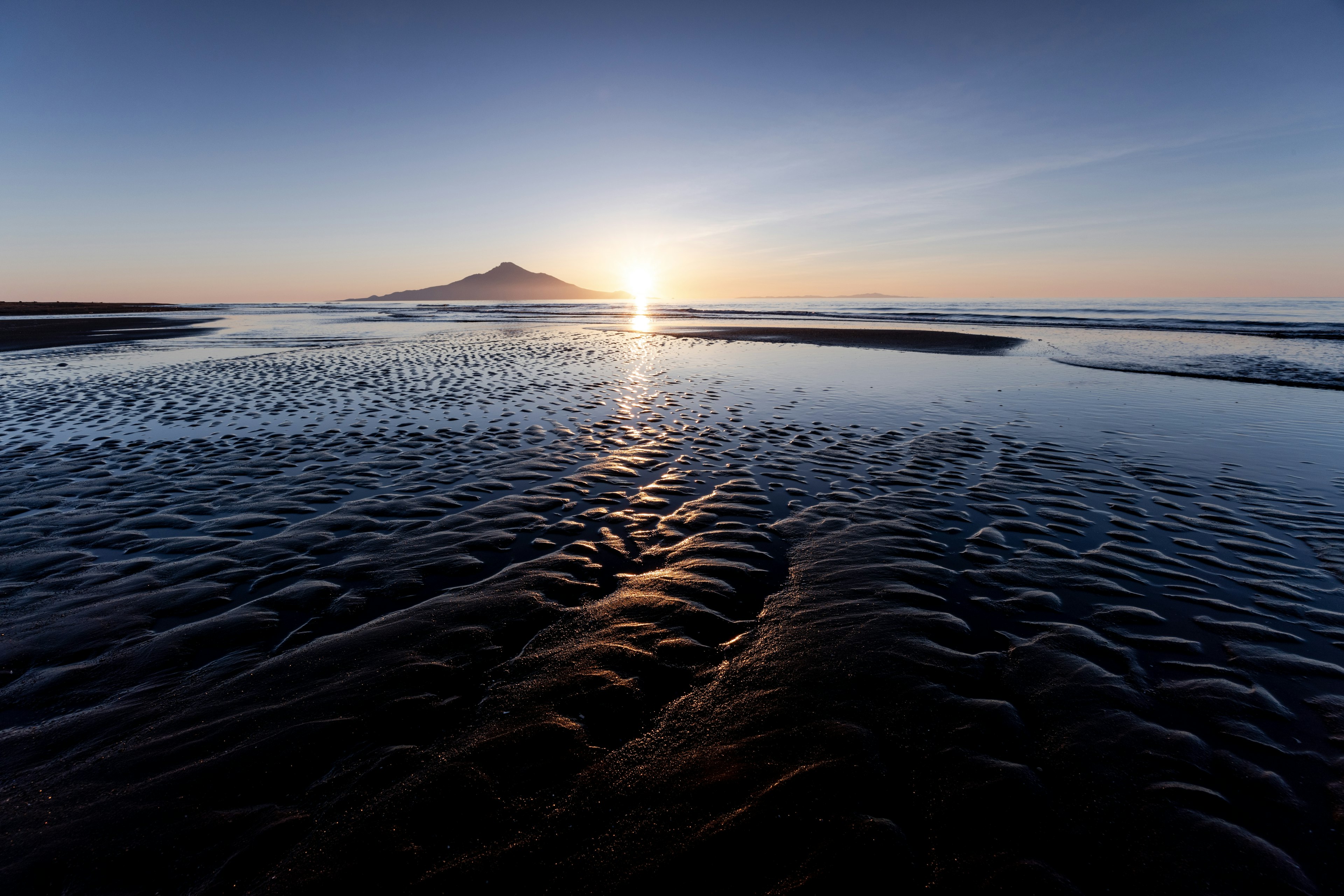 Sonnenuntergang über dem Ozean mit entfernten Bergen und nasser Sandtextur