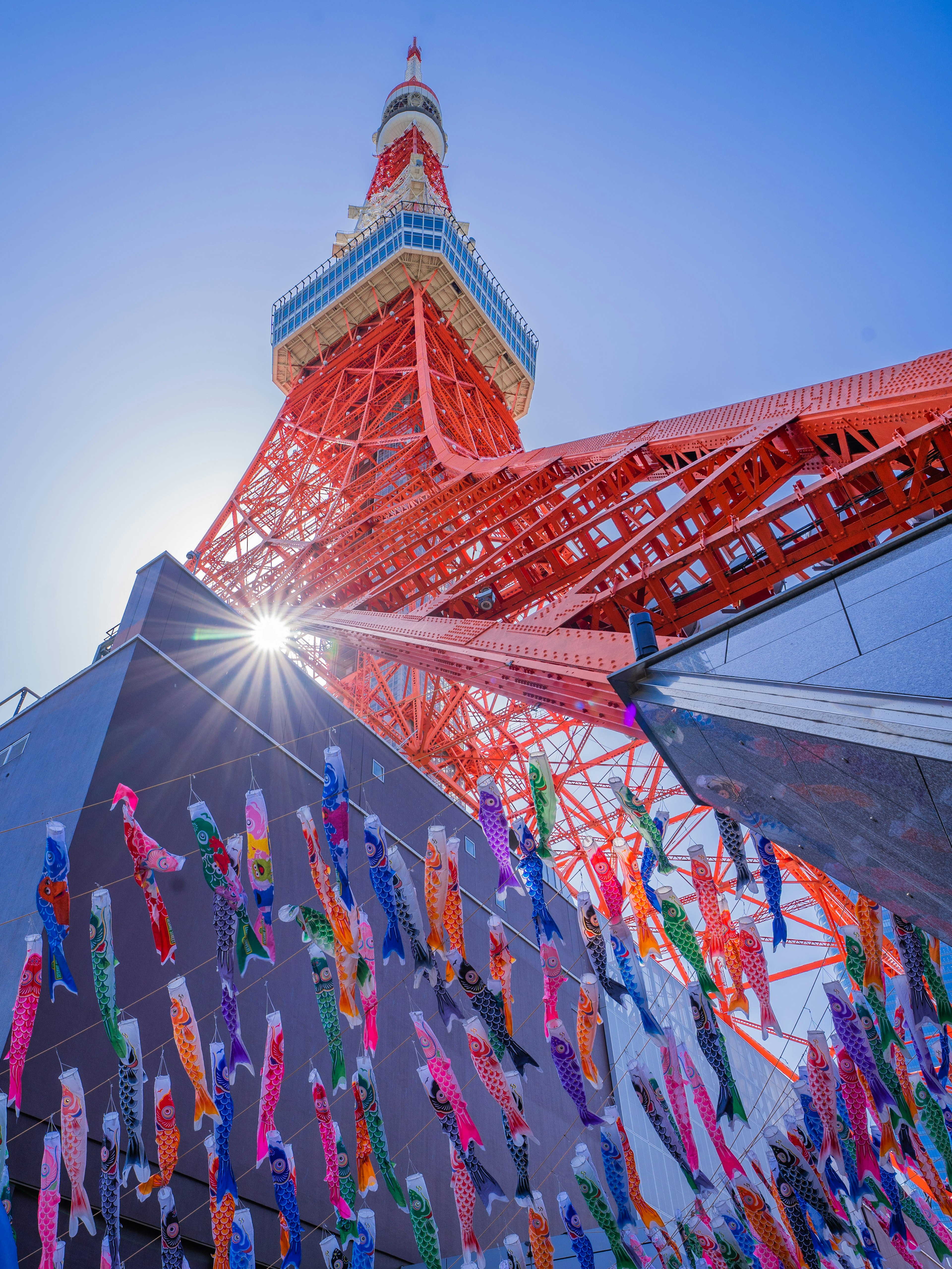 五彩缤纷的丝带装饰在东京塔底部，背景是明亮的蓝天