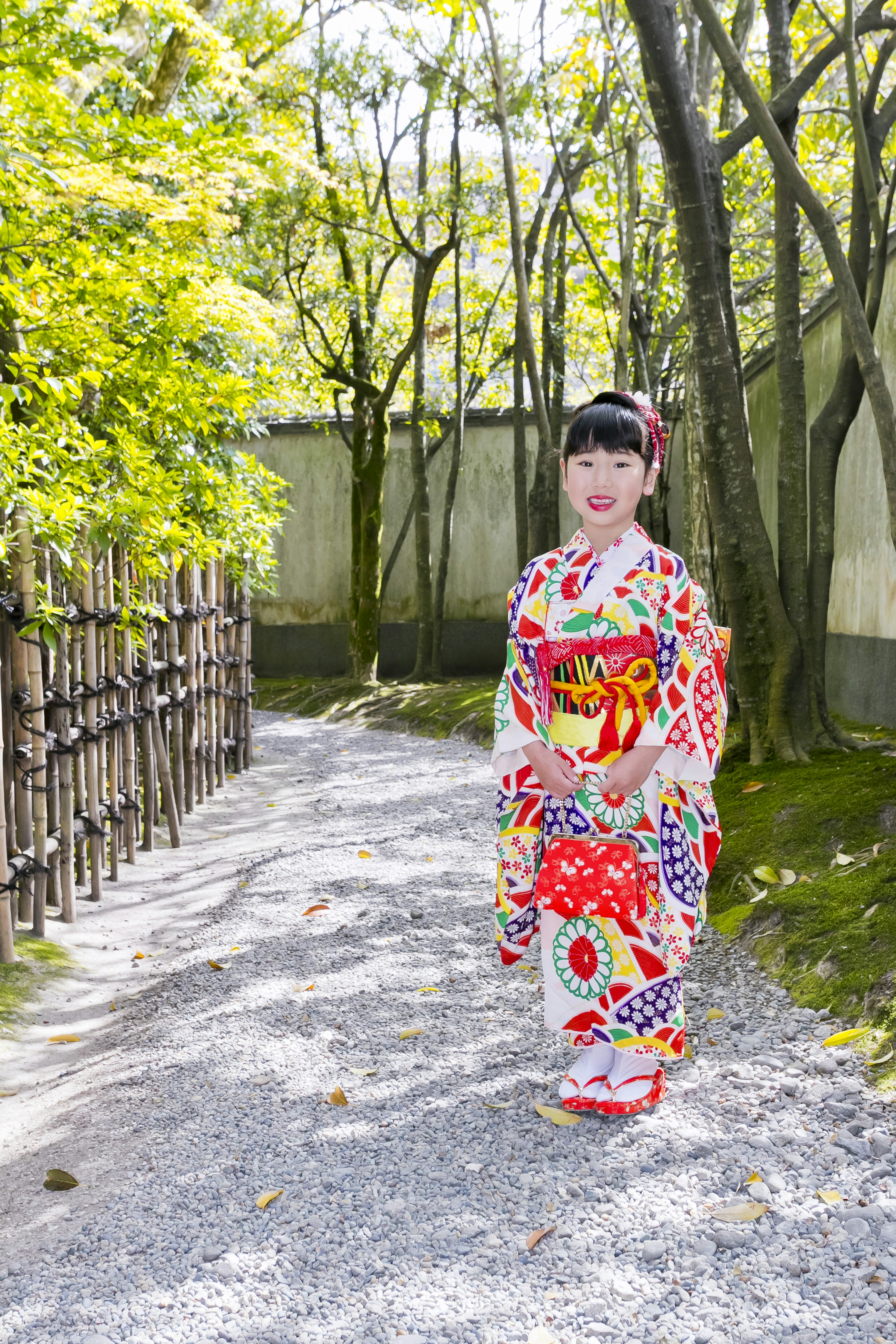 Eine Frau in einem schönen Kimono, die einen Weg entlanggeht, der von grünen Bäumen umgeben ist