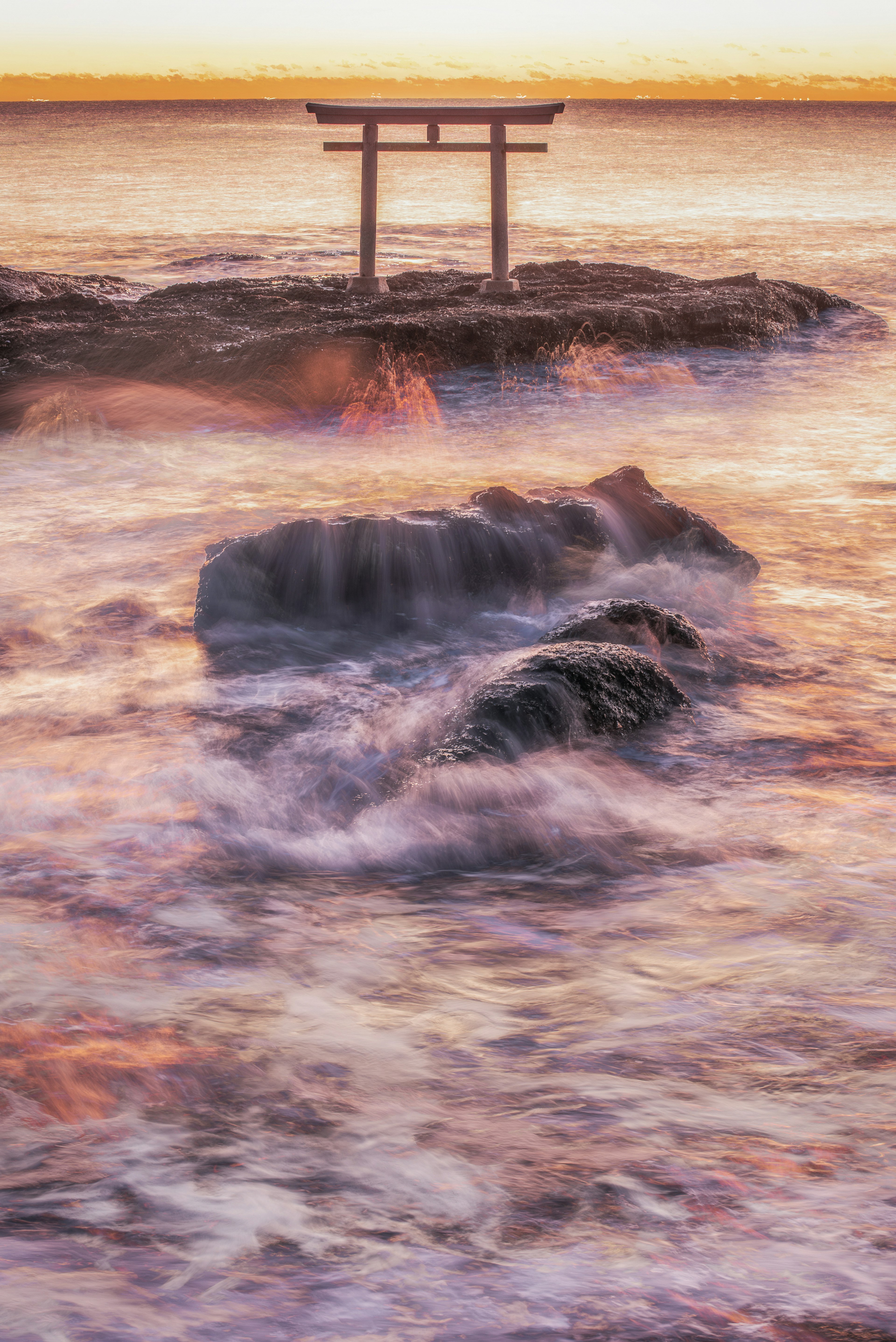 海の波と夕日を背景にした鳥居の写真