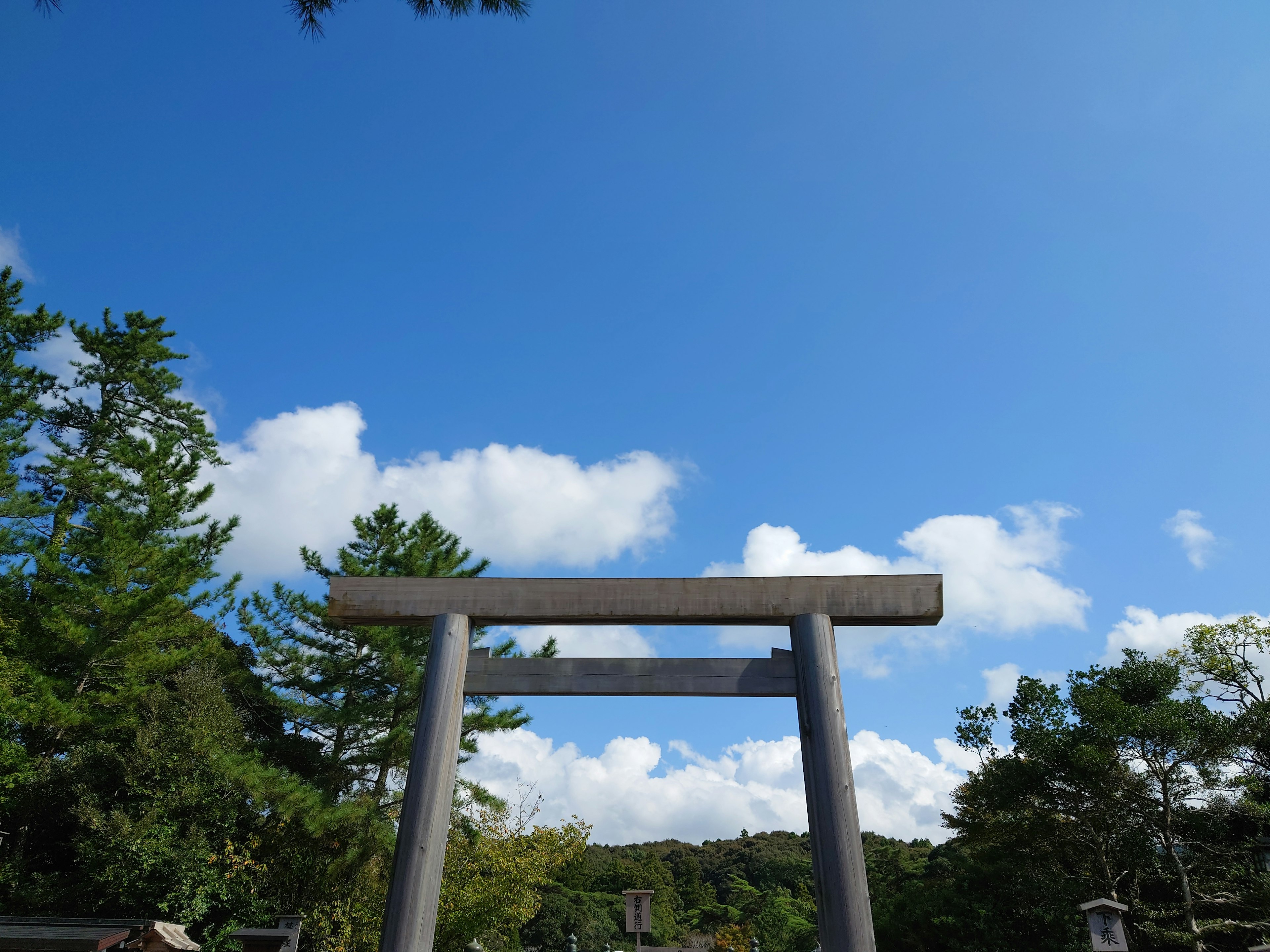 Torii-Tor unter einem blauen Himmel mit fluffigen Wolken und grünen Bäumen