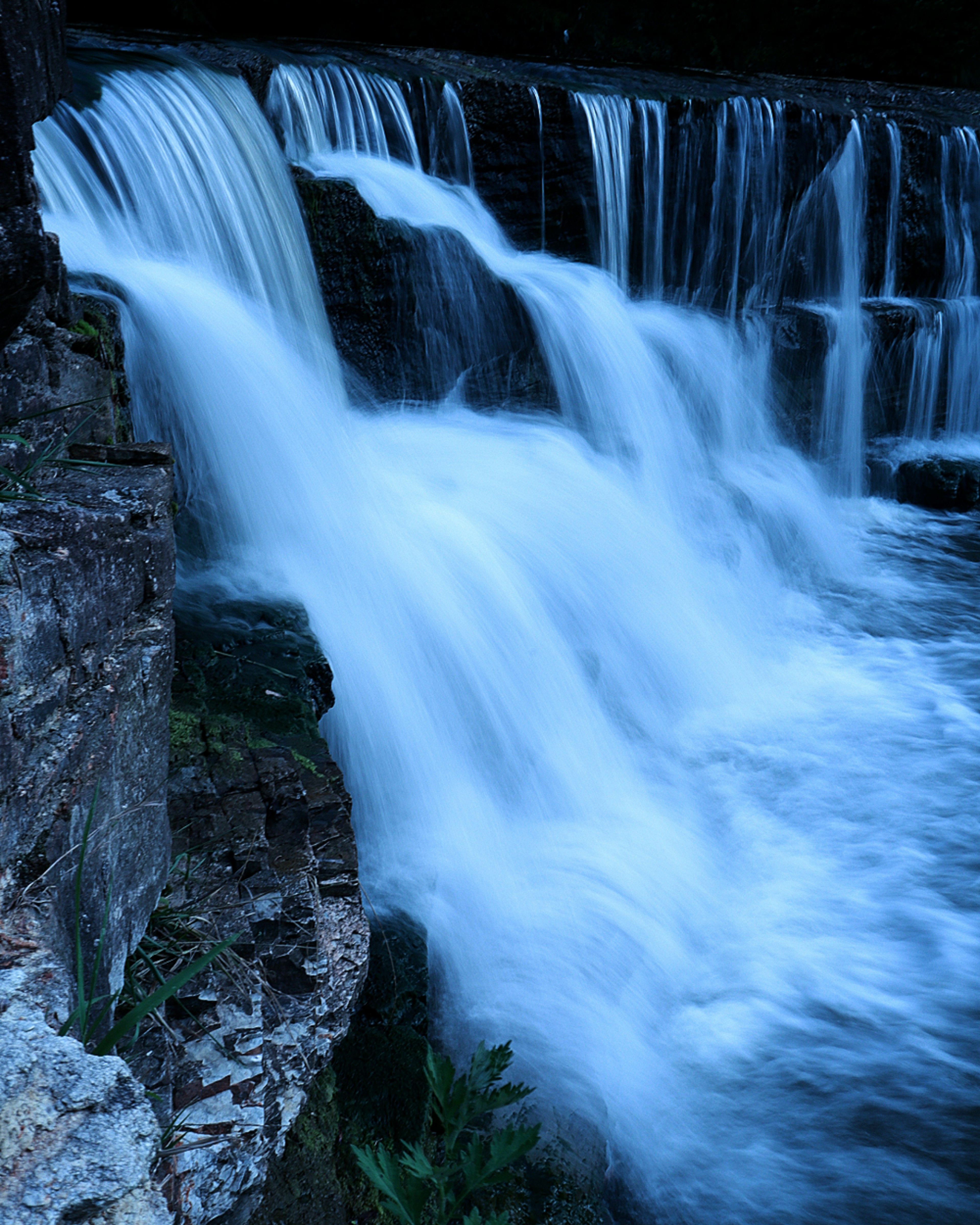 Imagen de una cascada con agua azul fluyendo sobre un terreno rocoso