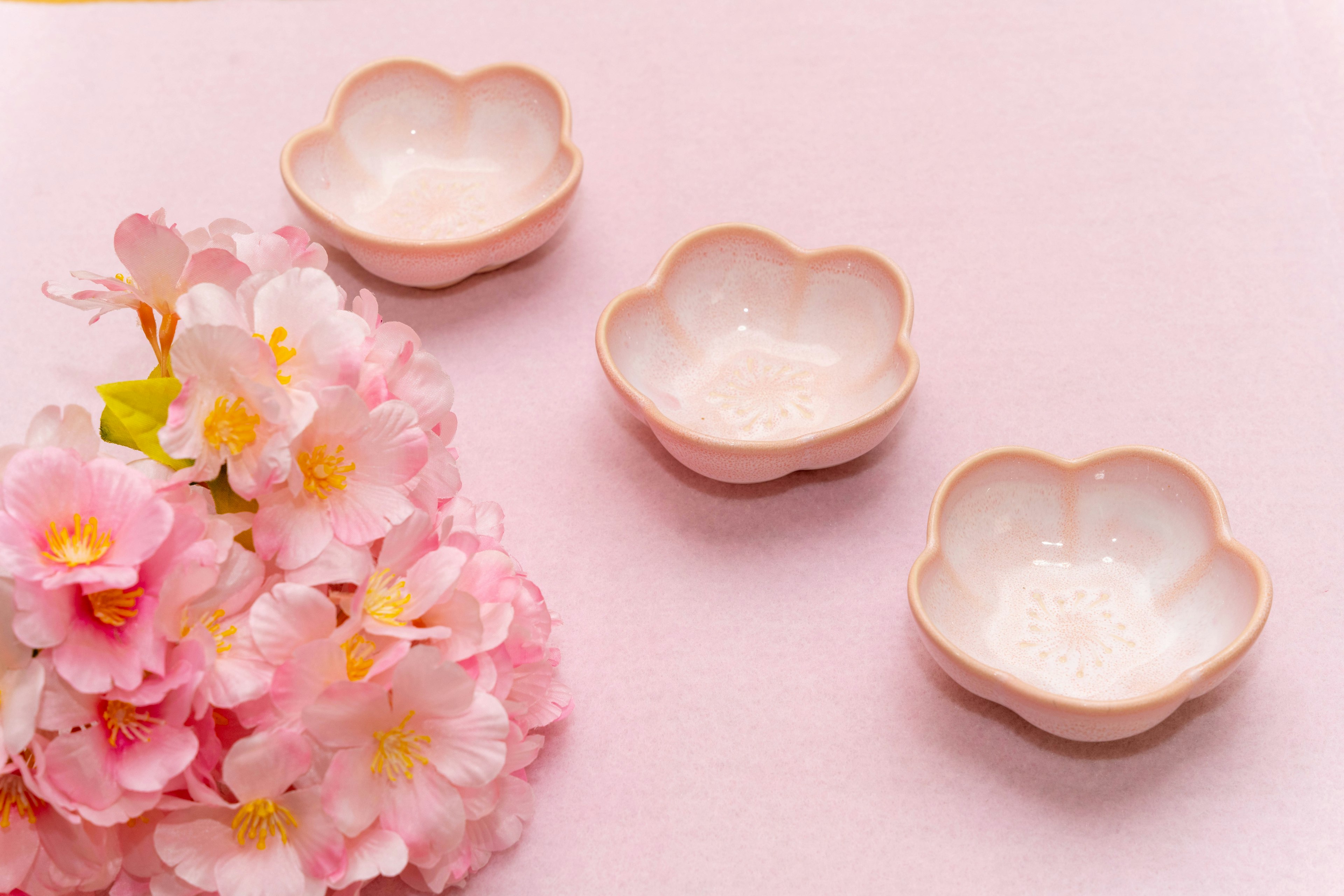 Tres pequeños platos en forma de pétalo cerca de flores de cerezo