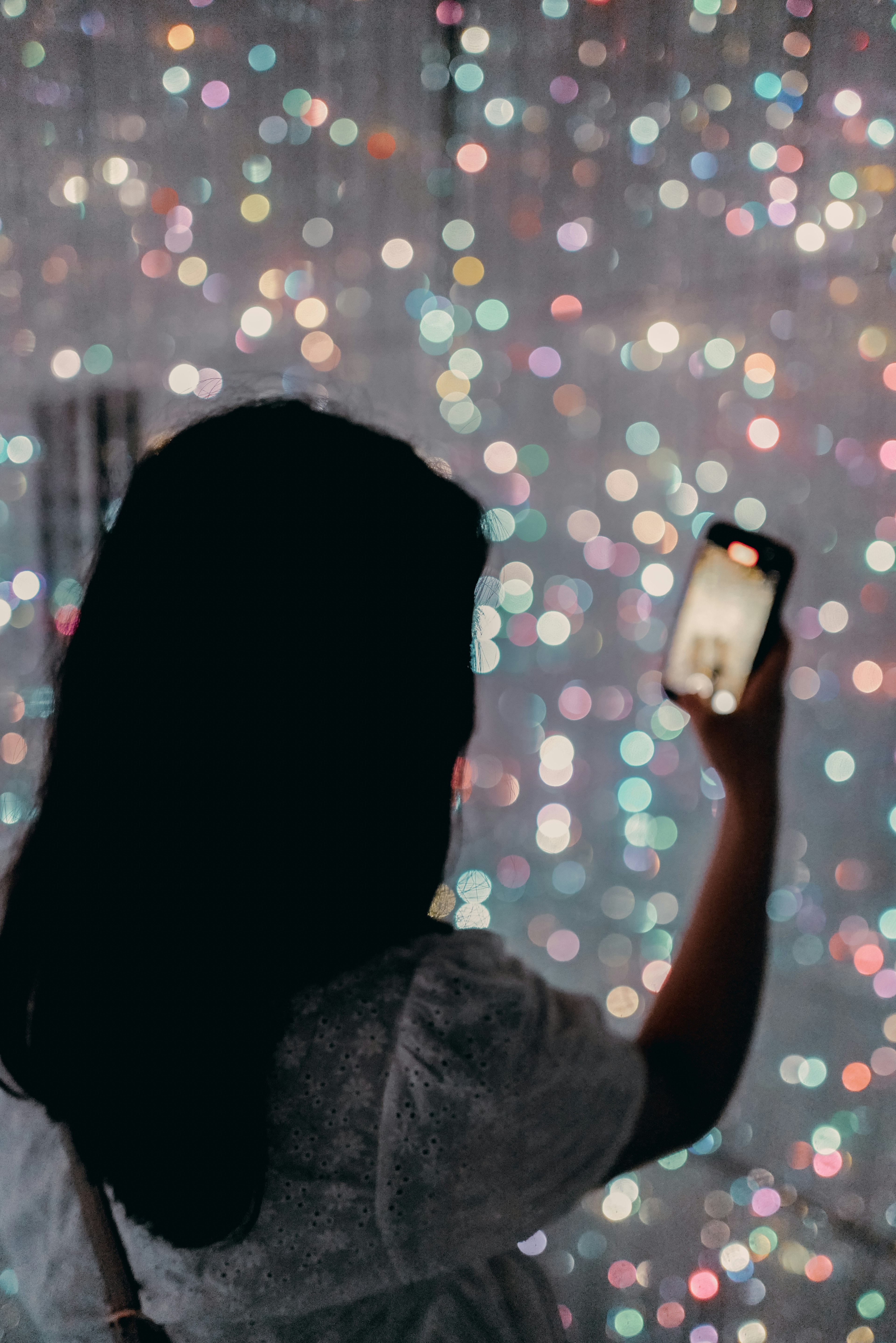 Silhouette wanita memegang smartphone dengan latar belakang lampu berwarna