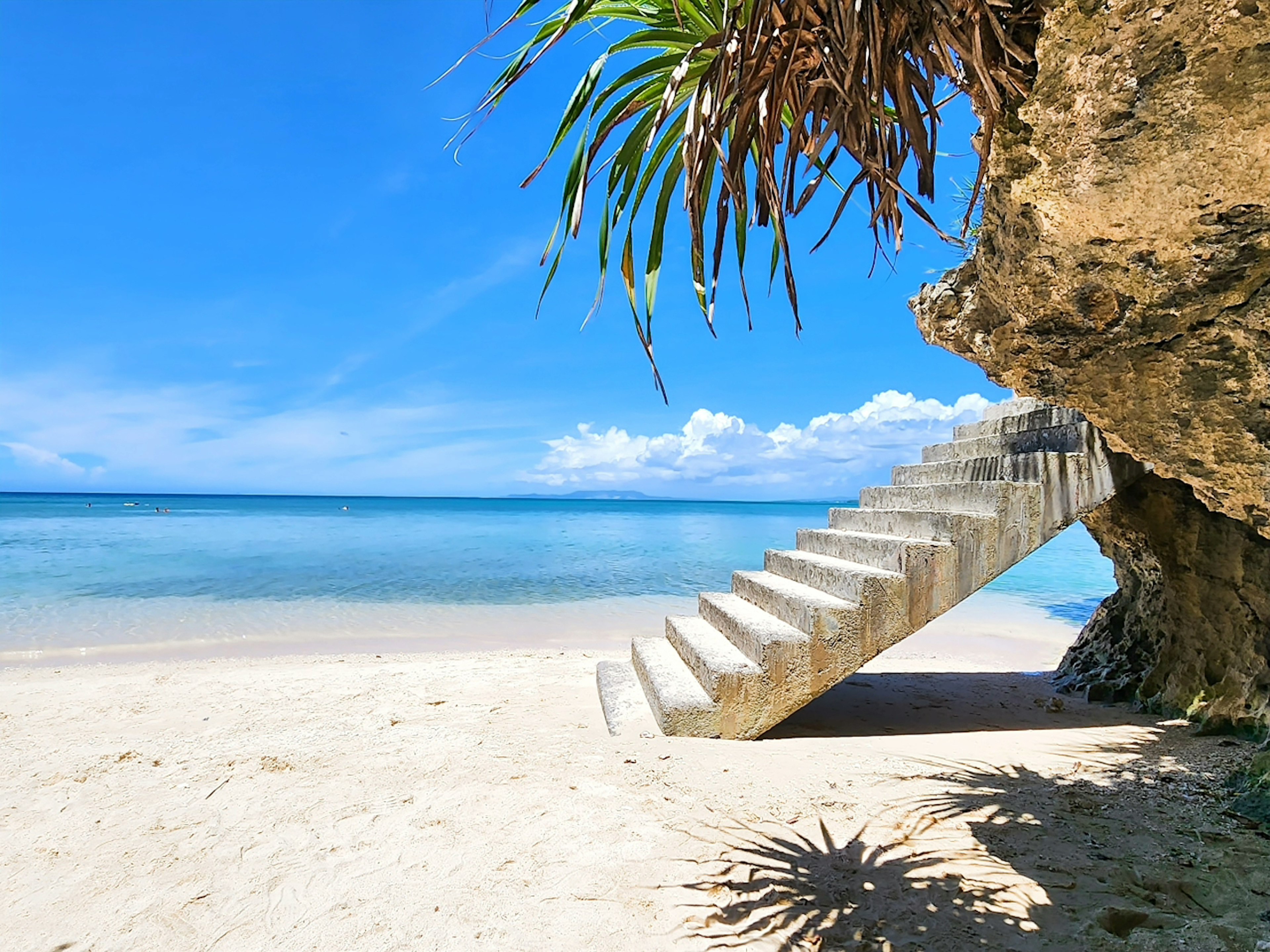 Escaliers en béton menant à une plage avec une eau et un ciel bleu clair