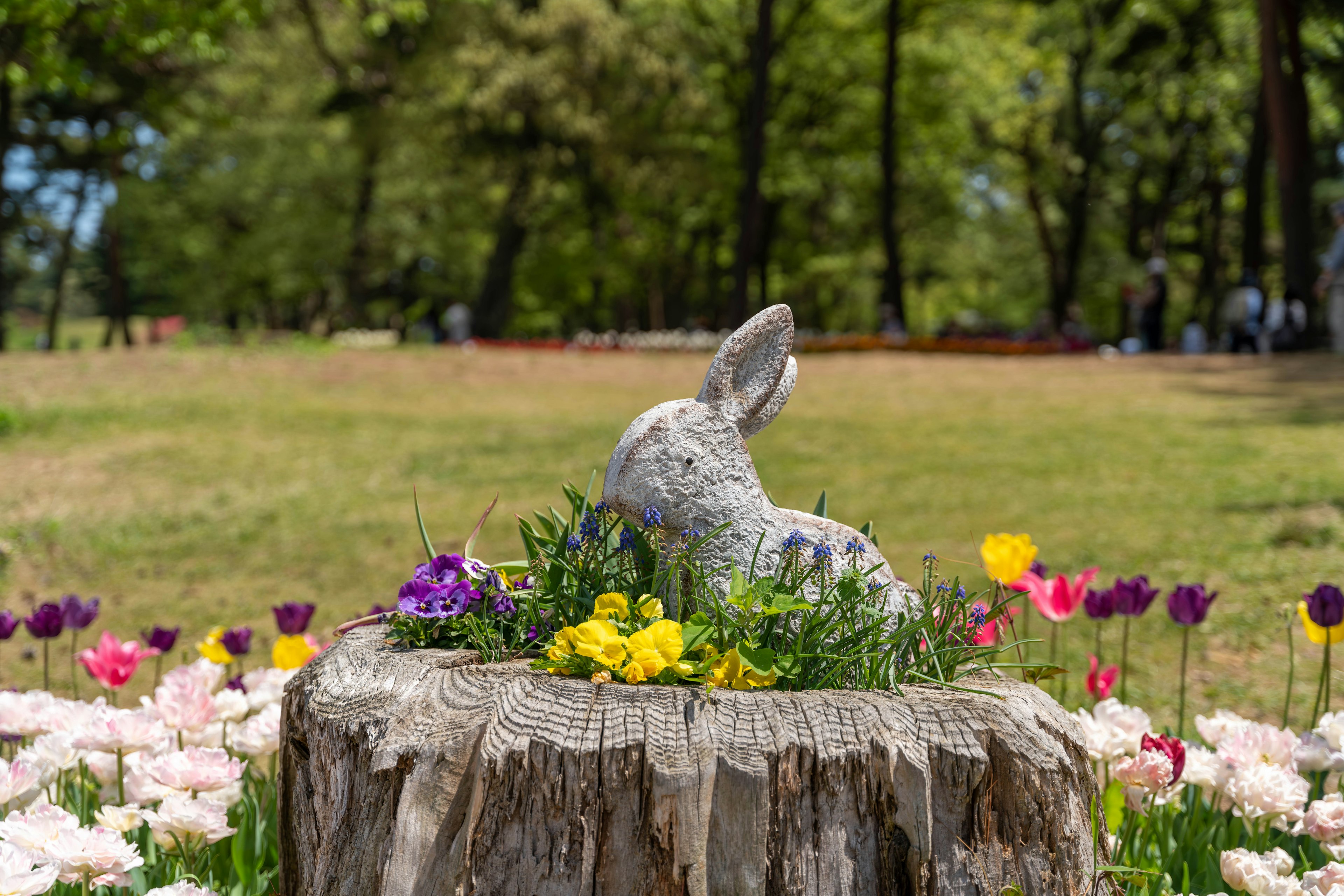 Sculpture de lapin sur une souche d'arbre entourée de fleurs colorées