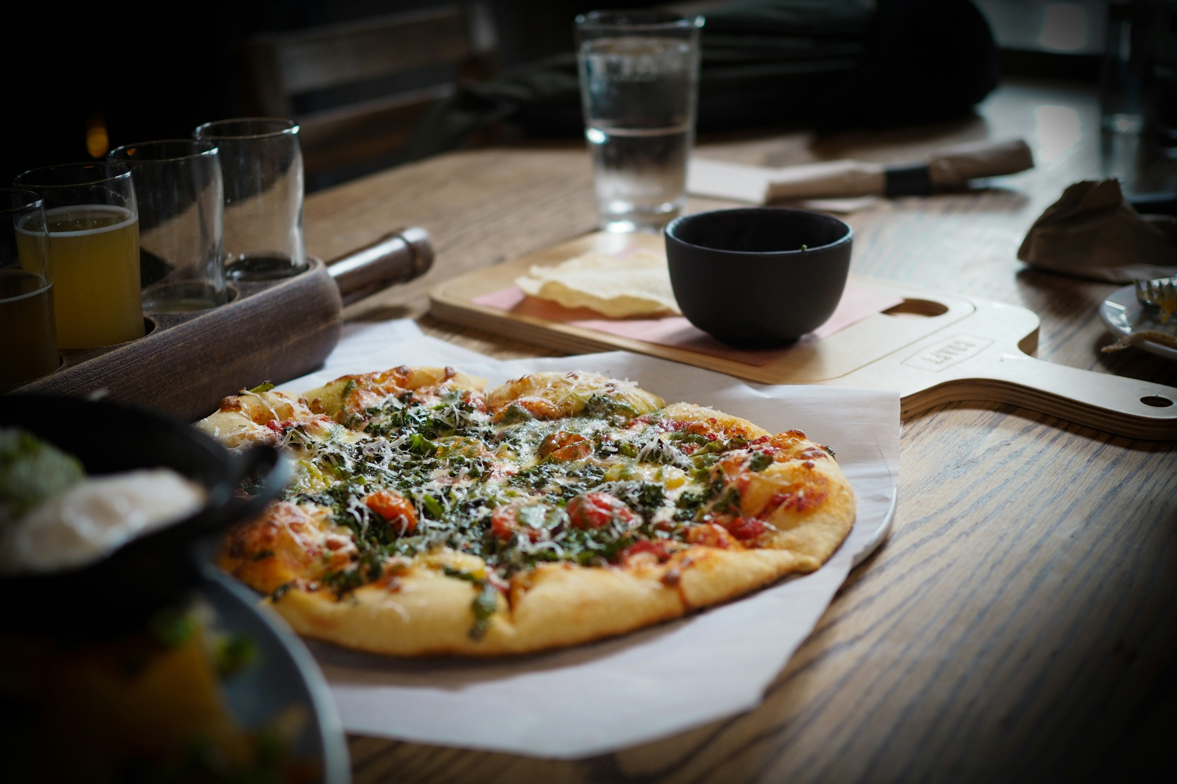 Pizza fresca su un tavolo guarnita con verdure e formaggio circondata da utensili da cucina e bevande