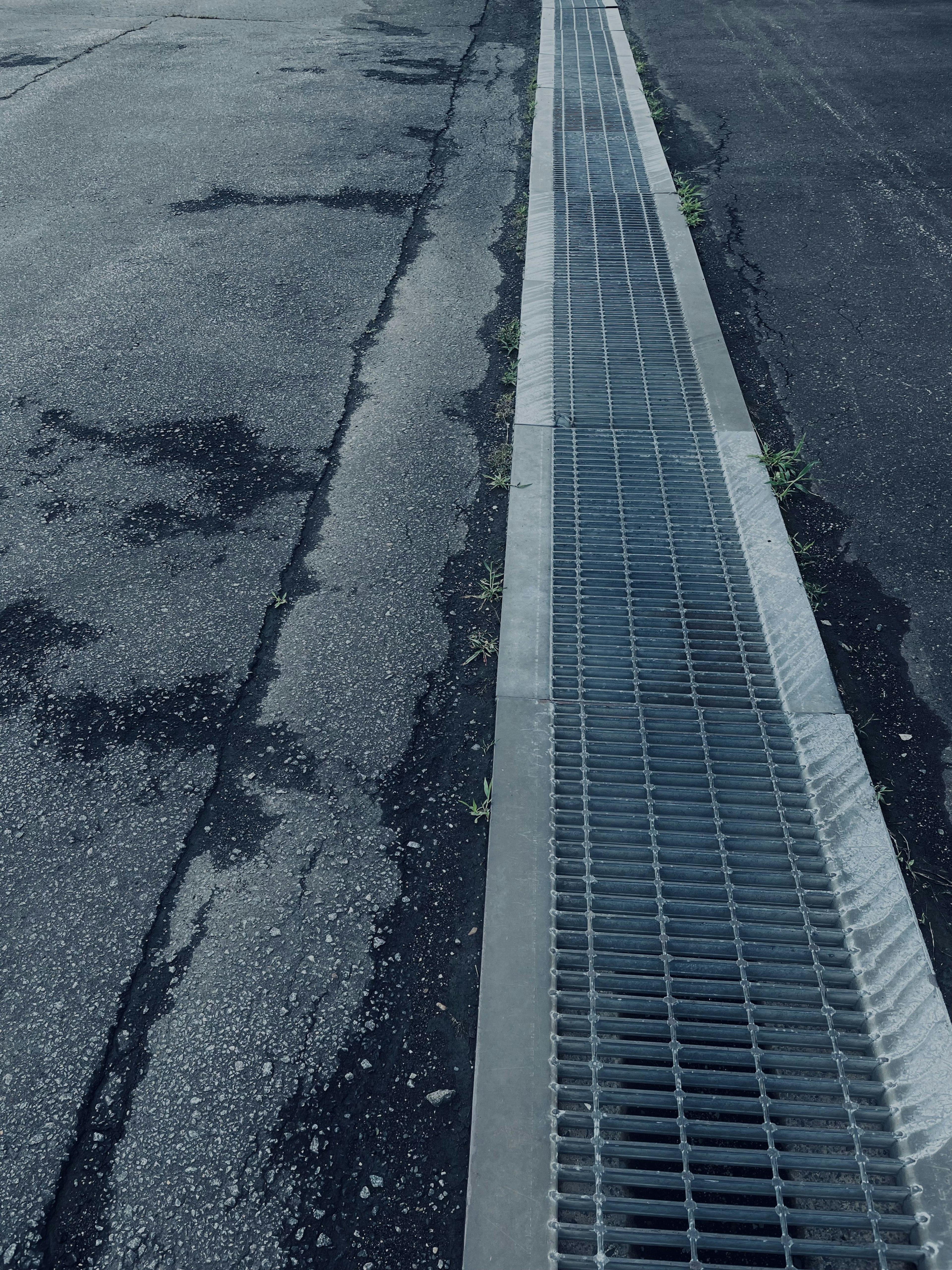 Metal grate along a cracked asphalt road showing wear and tear