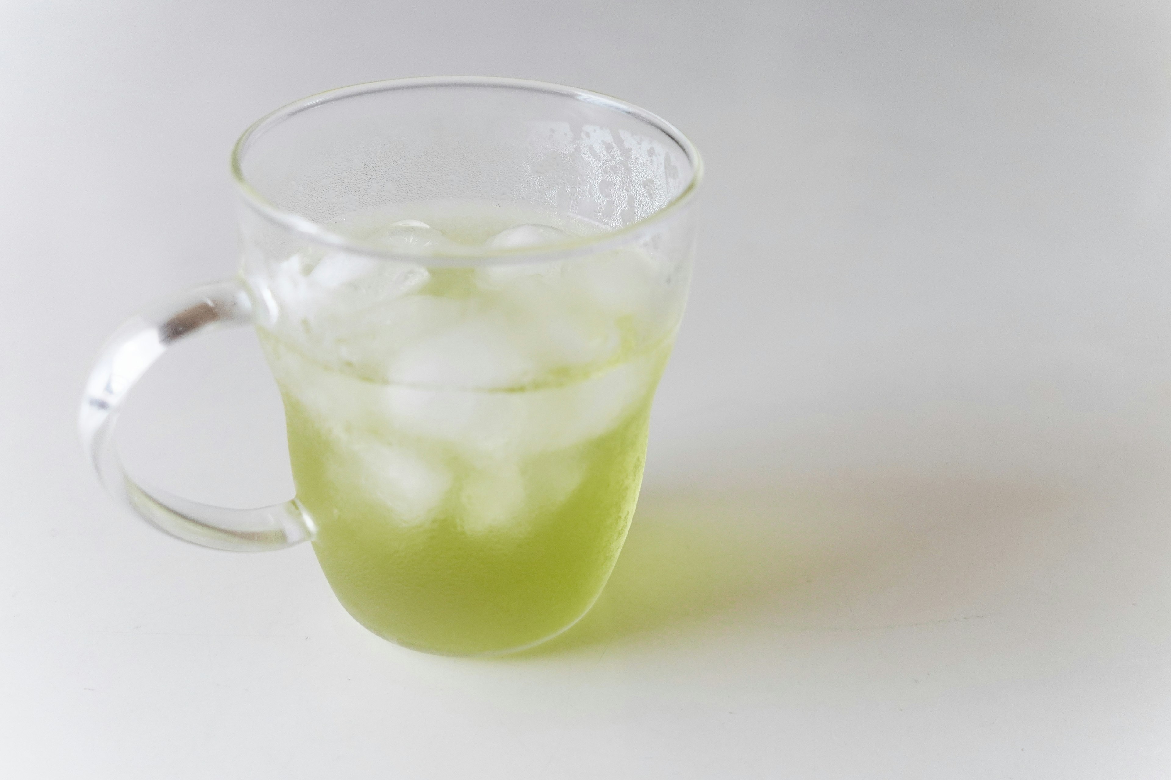 Transparent glass filled with green beverage and ice cubes