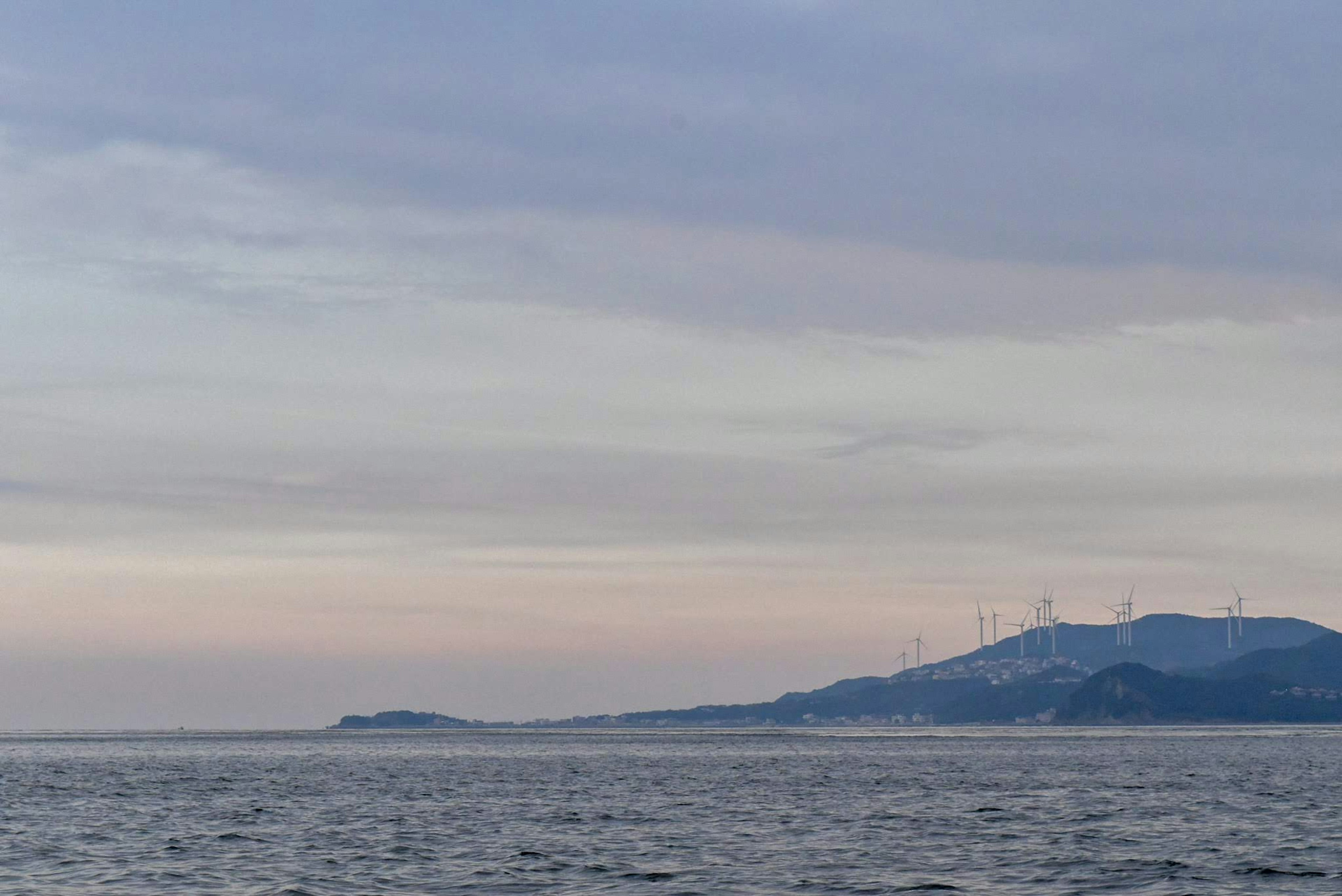 Ruhiges Meer mit Windkraftanlagen auf einem Berg