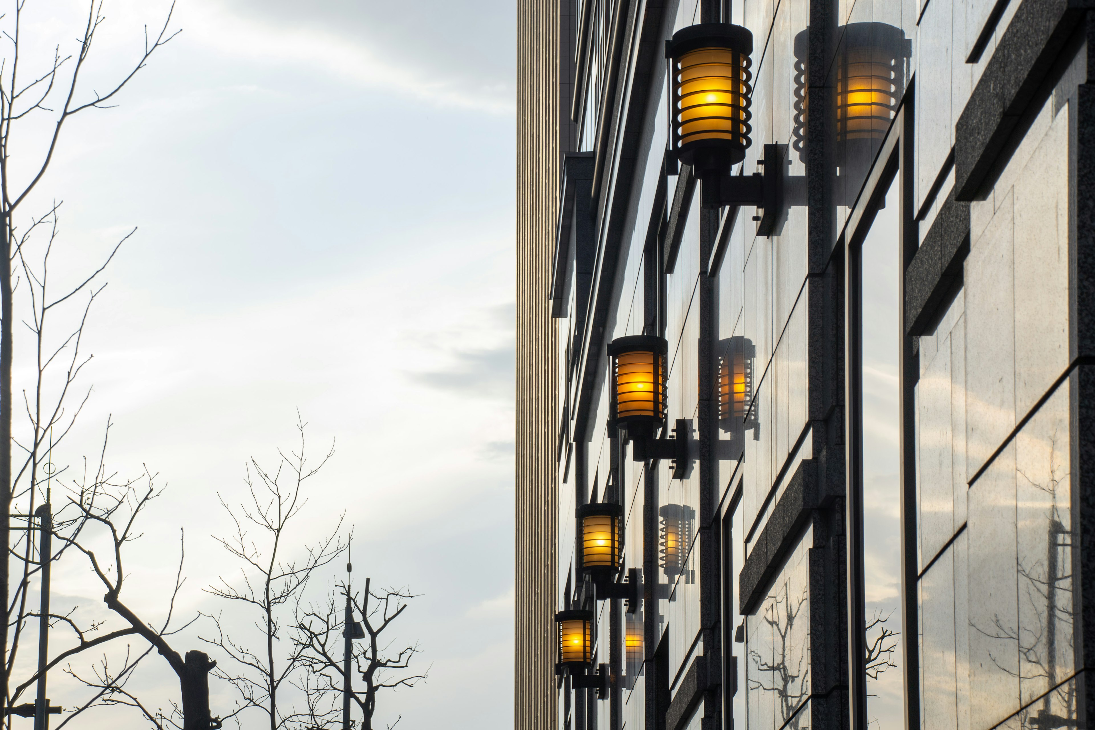 Row of wall-mounted lamps on a building exterior with cloudy sky