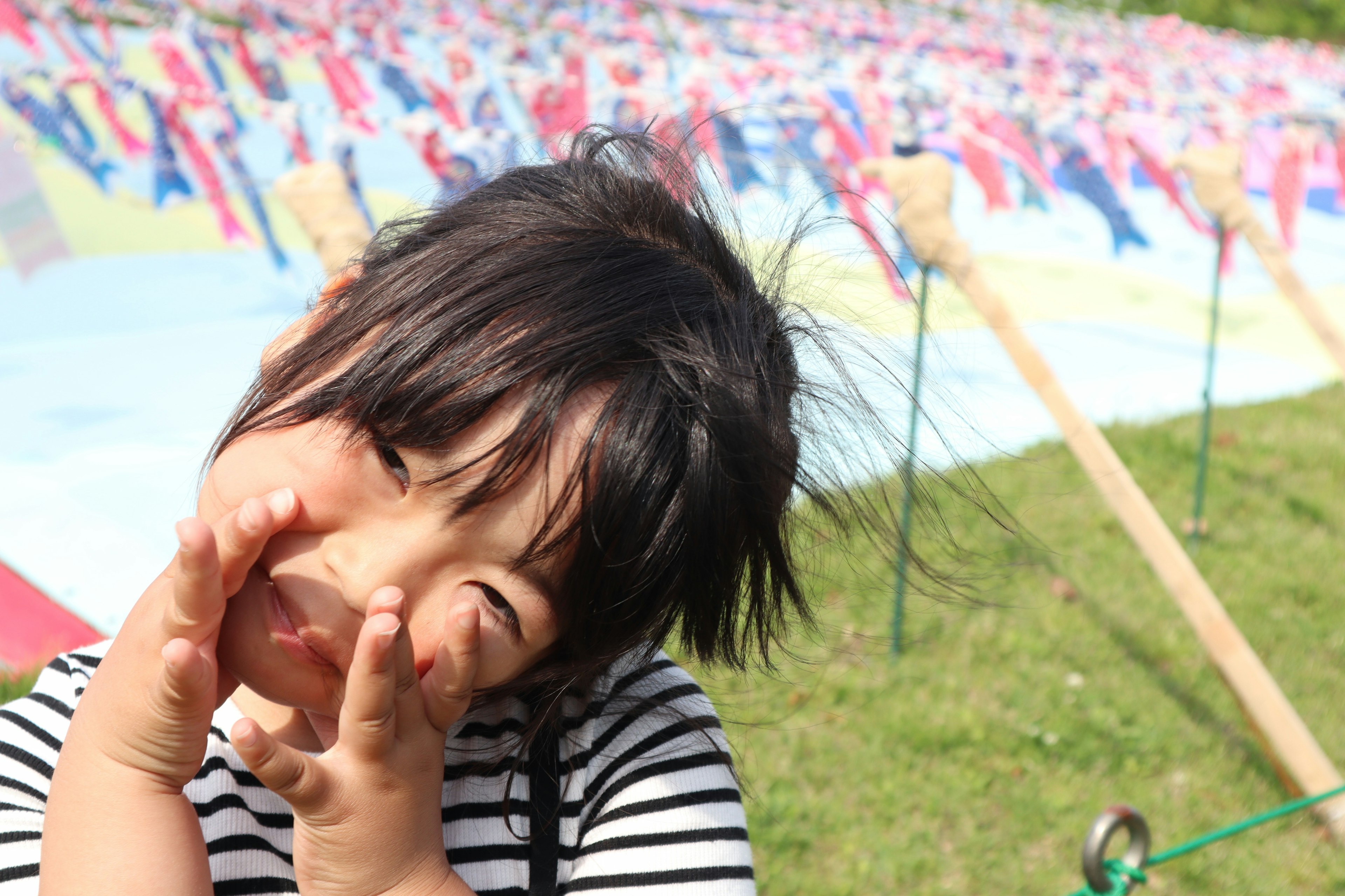 Un enfant portant un t-shirt rayé pose joyeusement avec un sourire devant un fond coloré de drapeaux