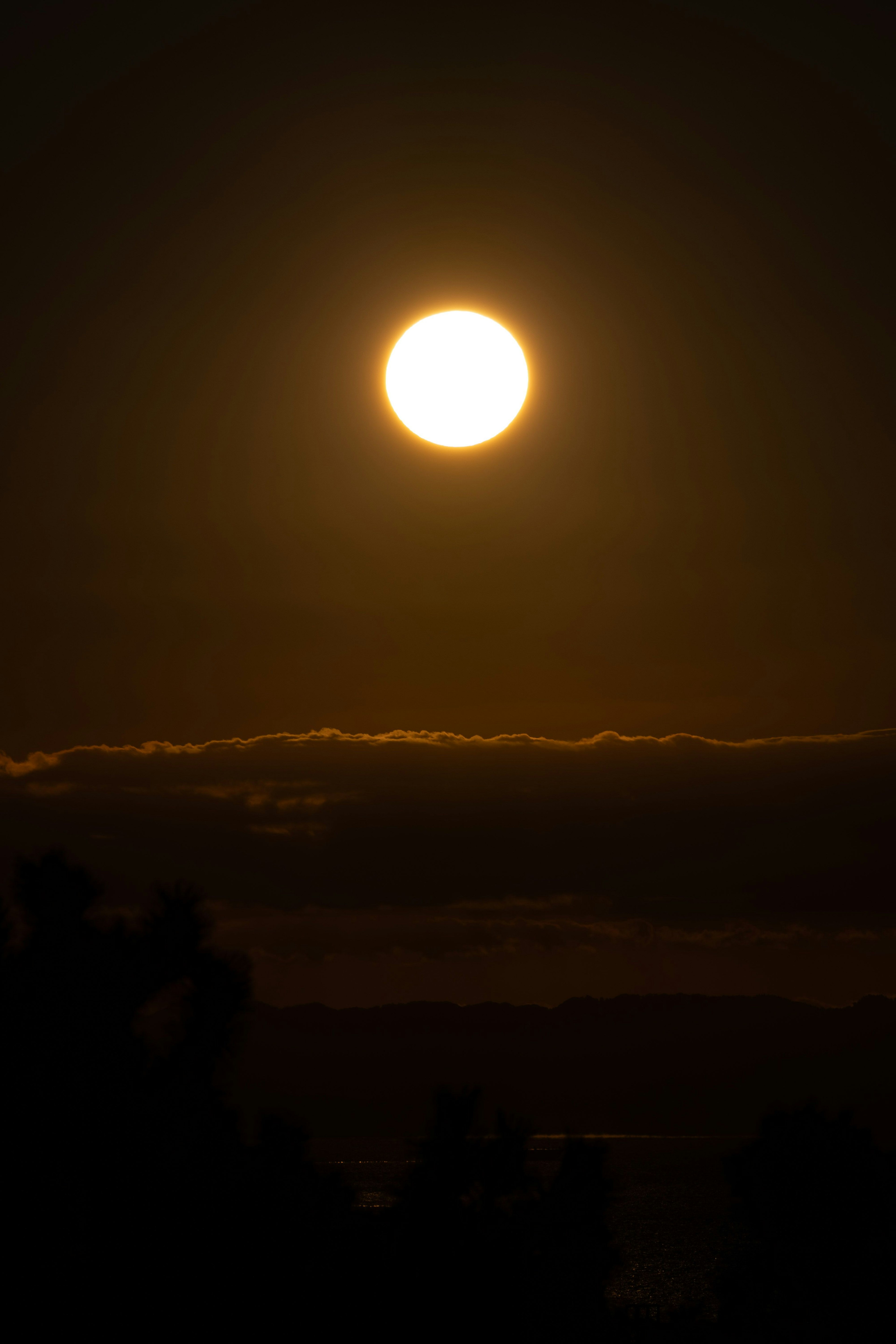 夕暮れの空に浮かぶ大きな太陽と雲のシルエット