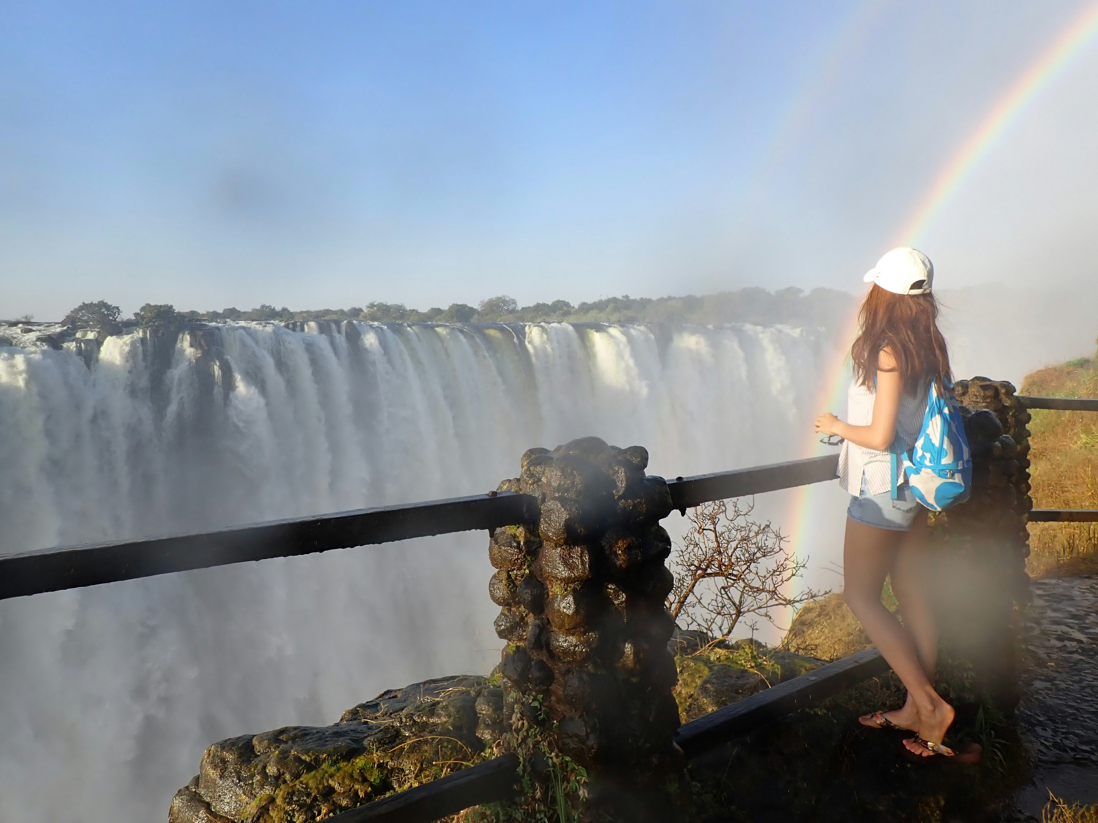 Frau steht neben einem Wasserfall mit einem Regenbogen im Hintergrund