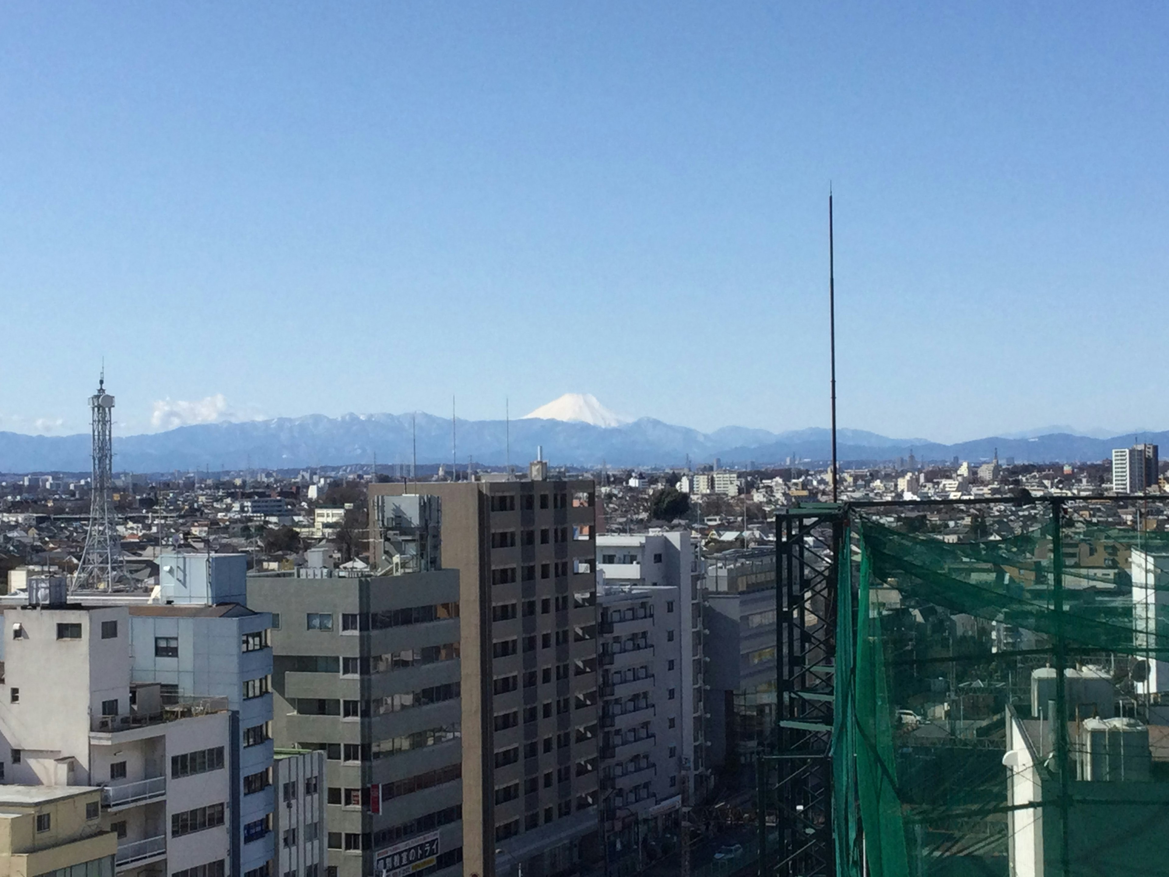 青空の下に広がる都市の景観と雪をかぶった山々