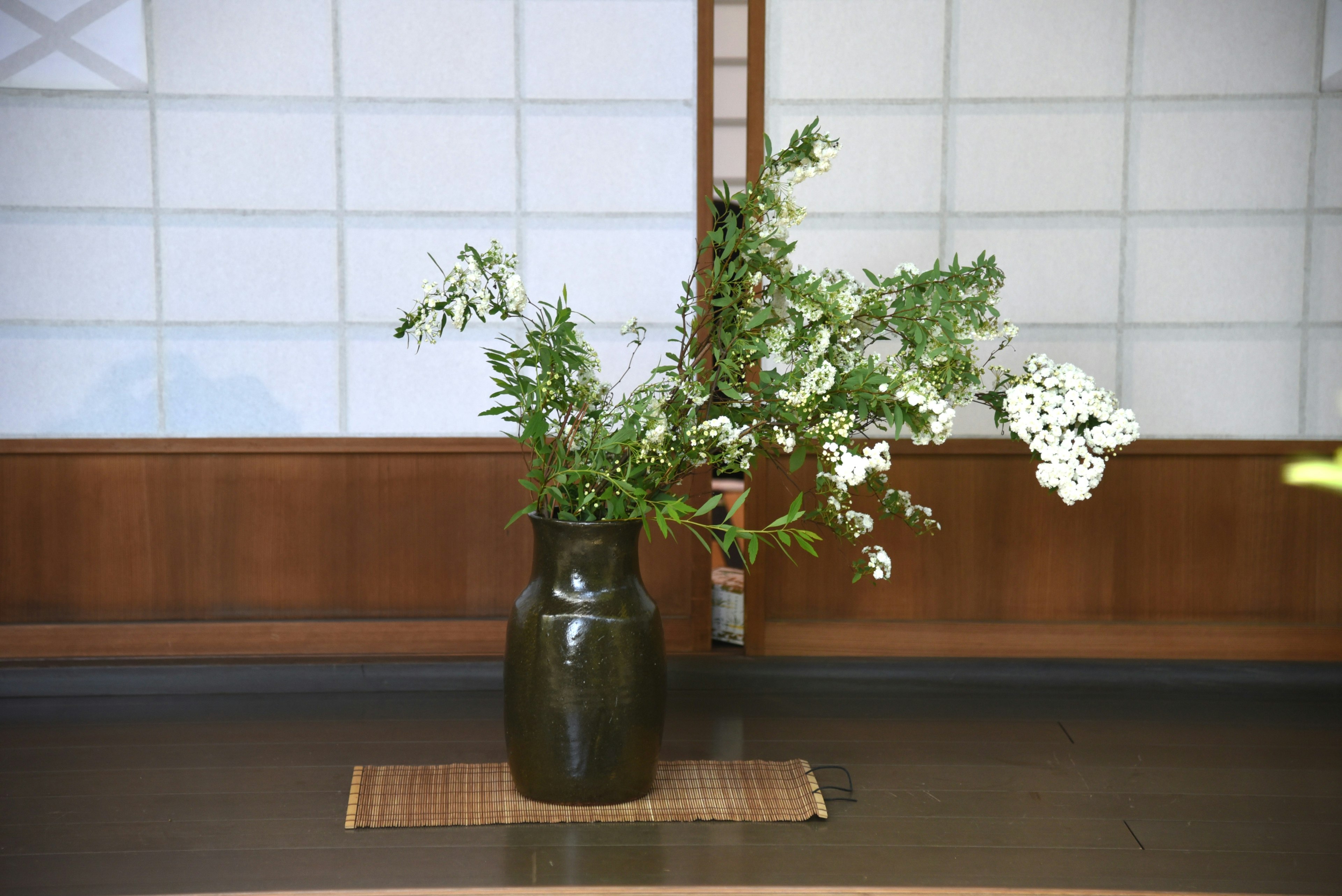 A black vase with white flowers and green leaves in a Japanese interior