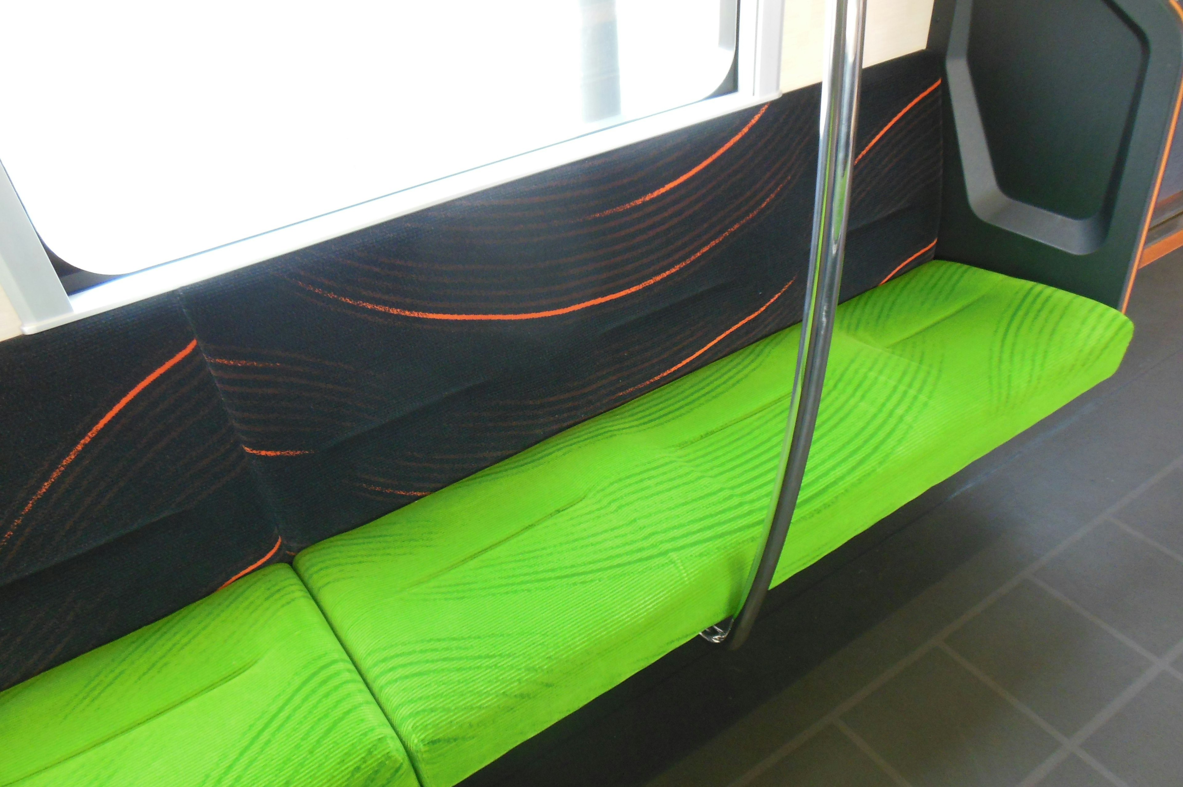 Interior de un vehículo de transporte público con un asiento verde brillante y una pared negra