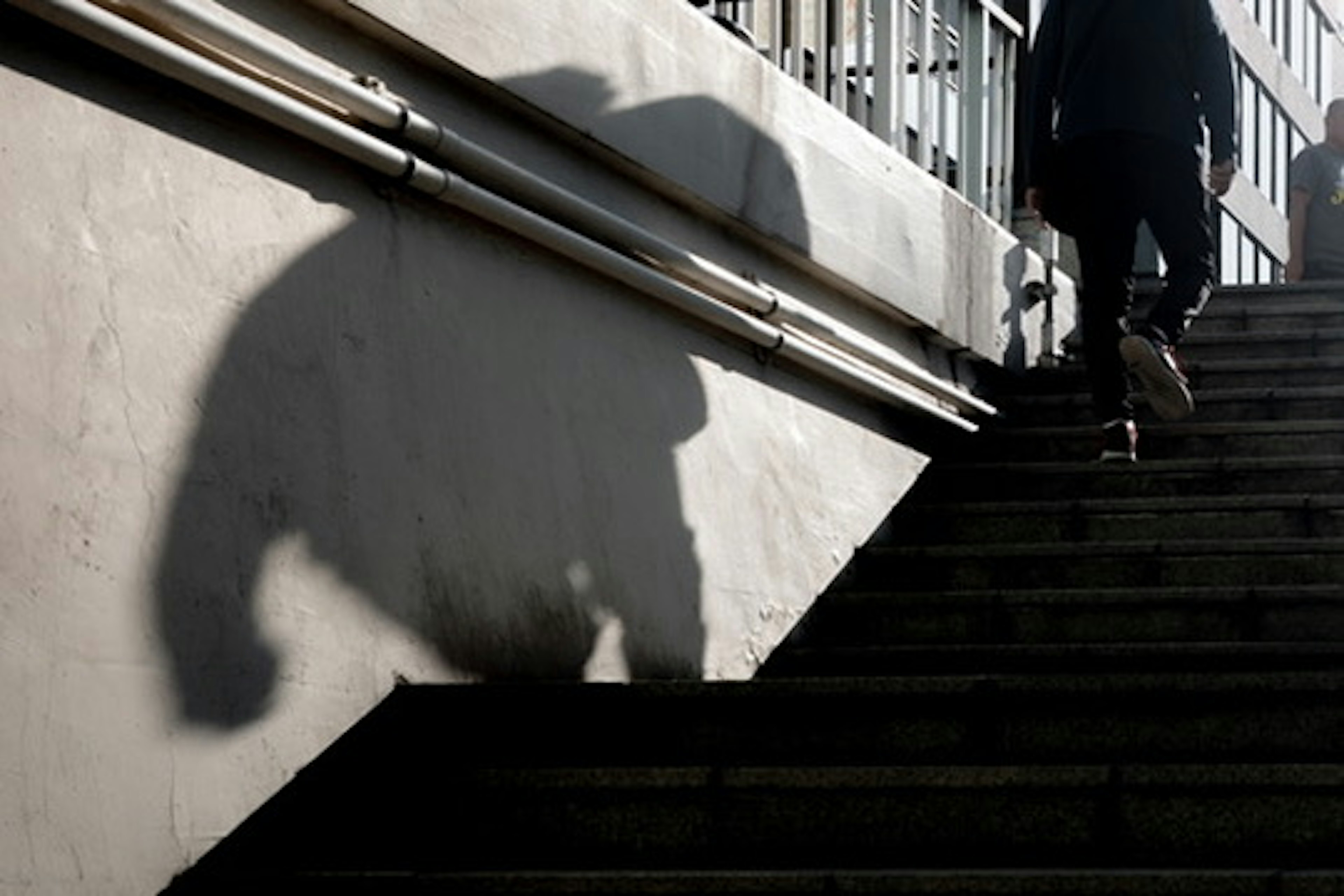 Silhouette of a person walking up stairs with a shadow on the wall