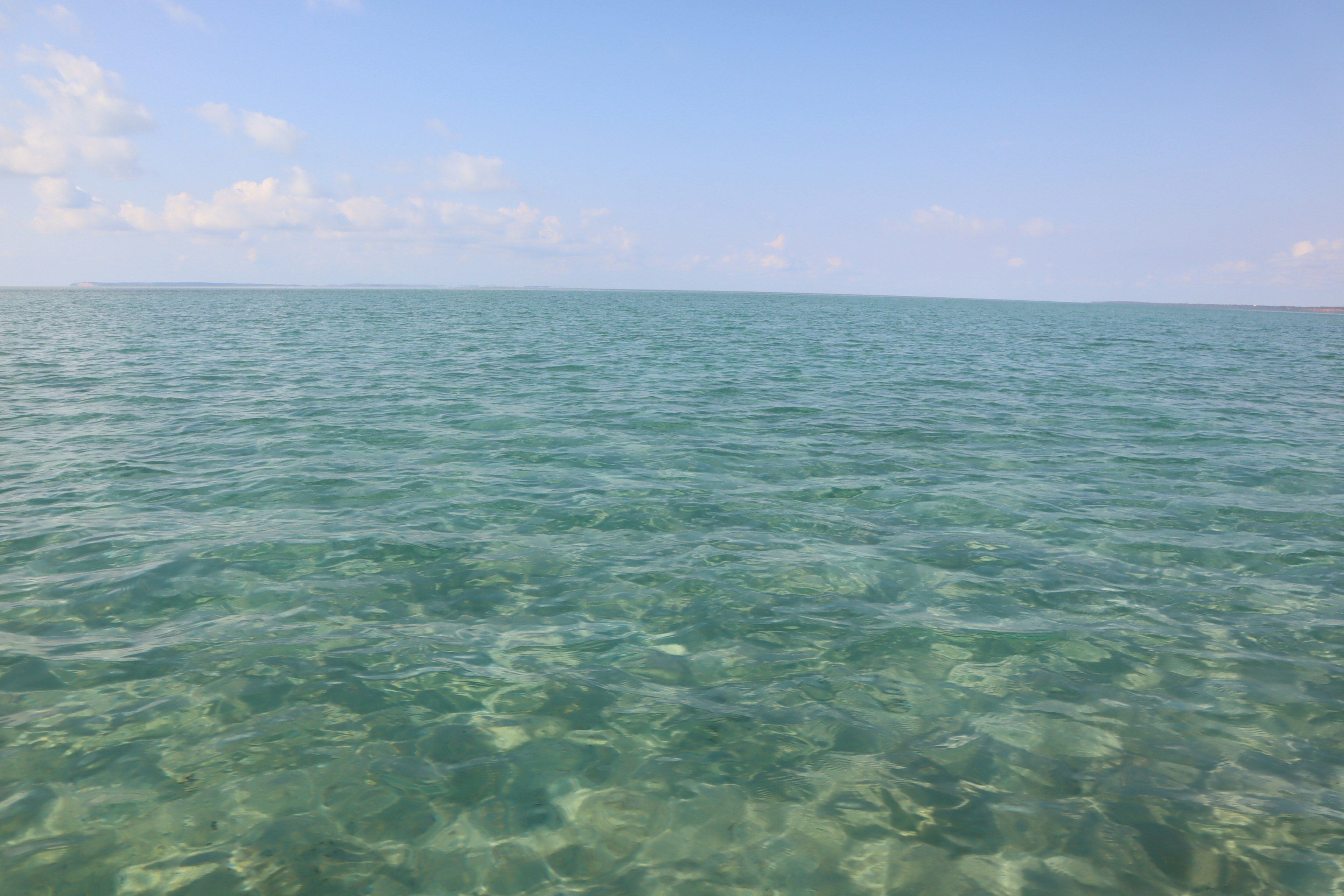 Pemandangan tenang lautan biru dan langit dengan permukaan air yang tenang dan jernih