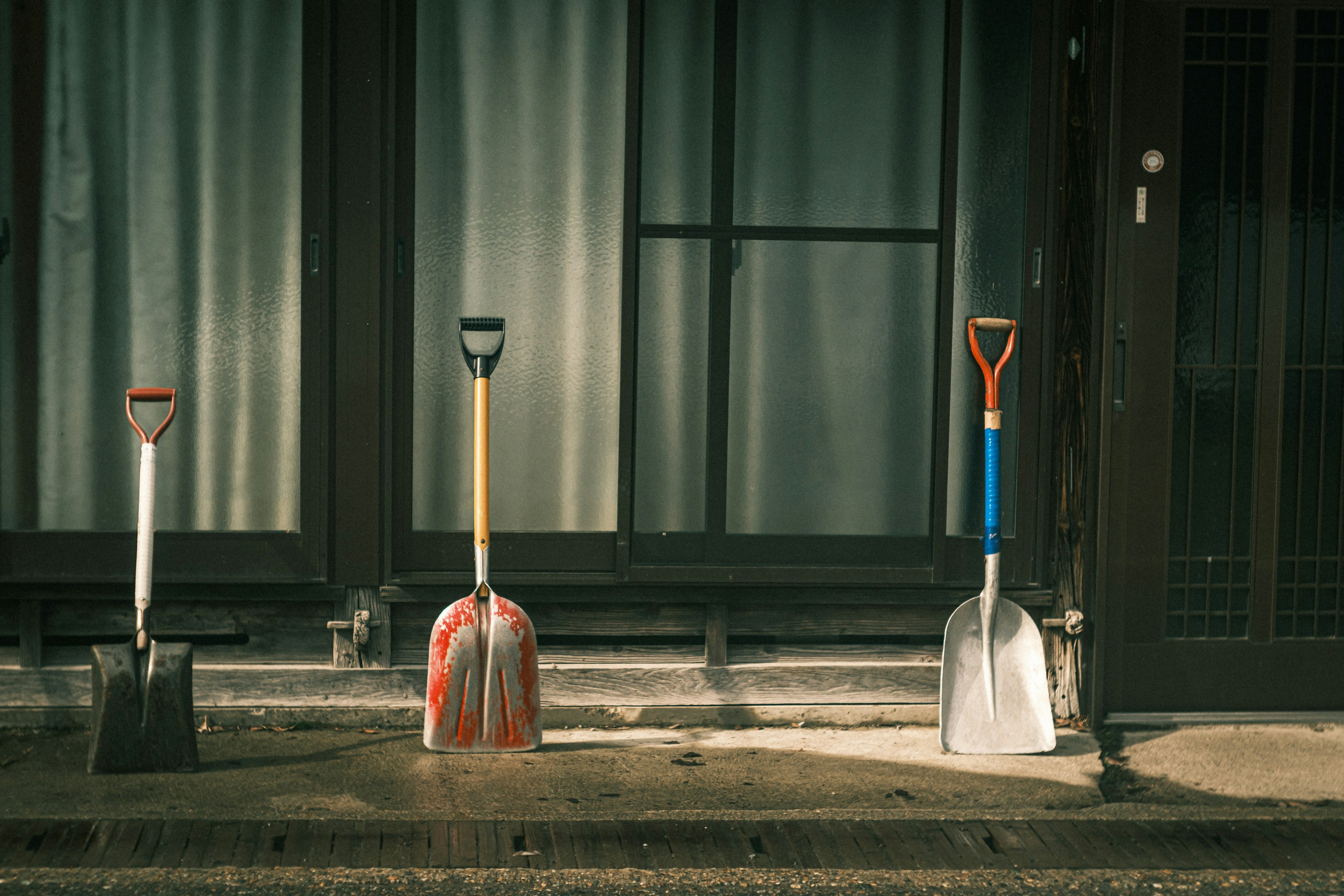 Three shovels lined up in front of a doorway with sunlight casting shadows