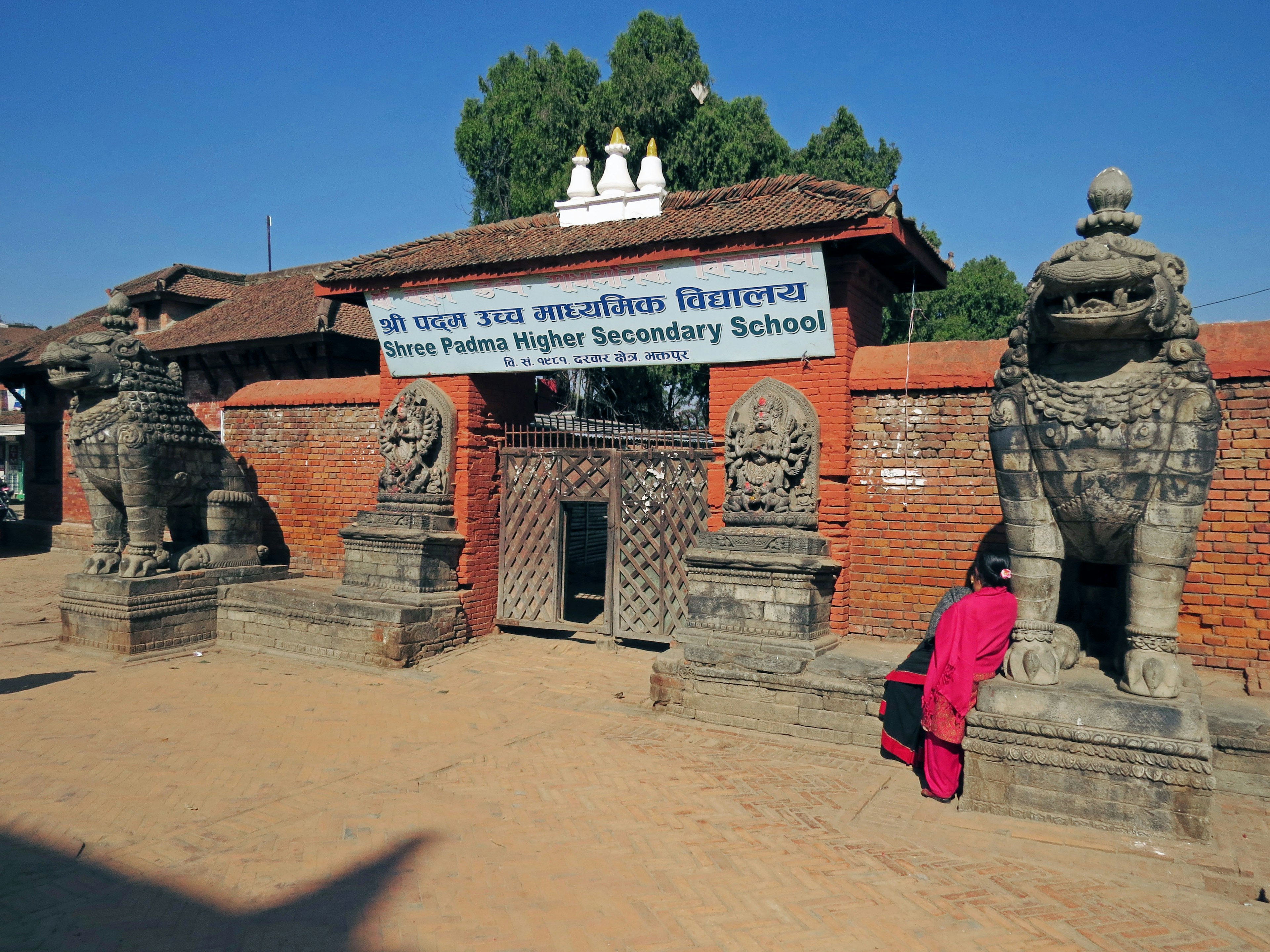 Eingang zu einer Sekundarschule mit zwei Löwenstatuen und einer roten Backsteinmauer