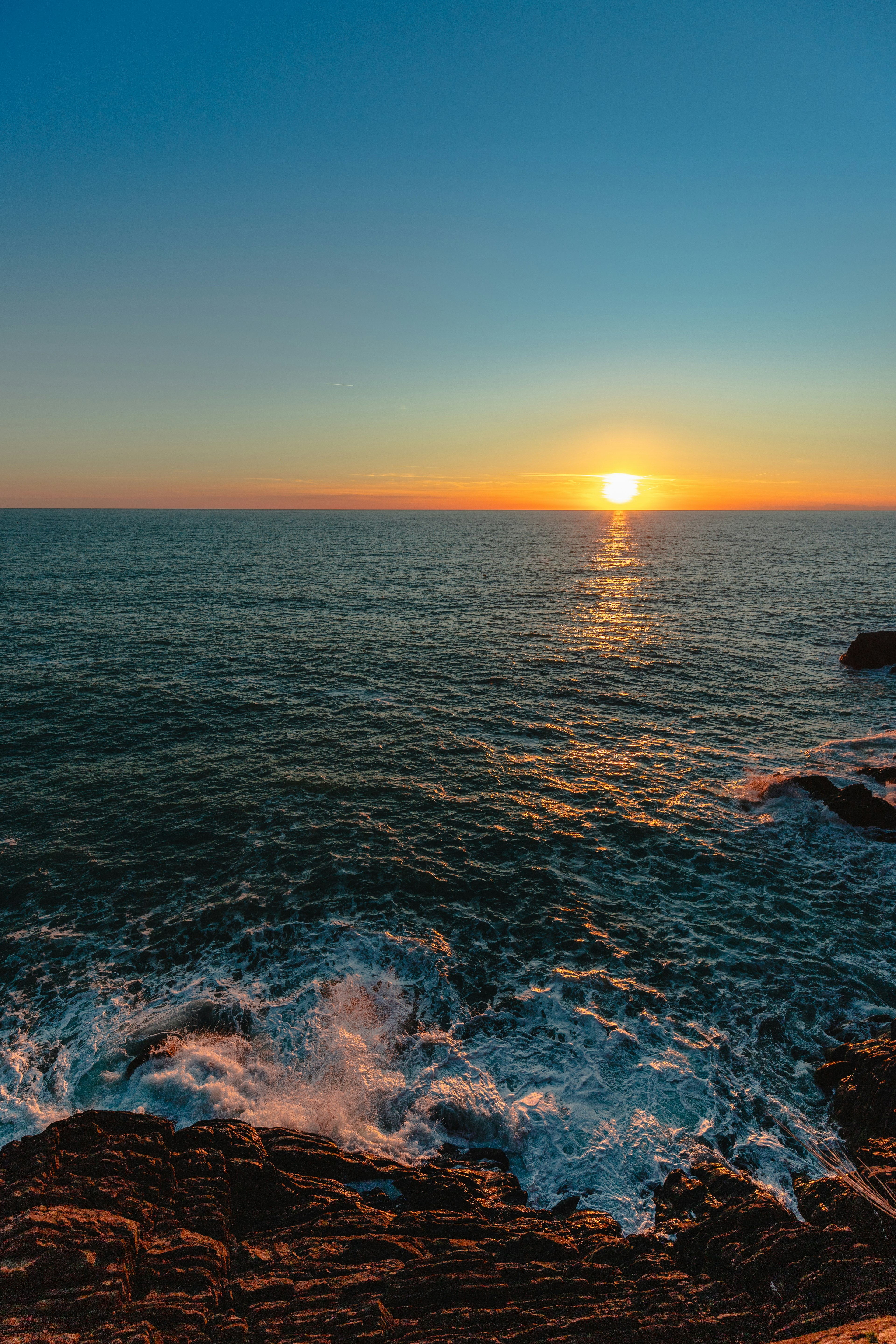 Beautiful sunset viewed from rocky coastline gentle waves lapping against the shore clear blue sky with colorful sunset hues