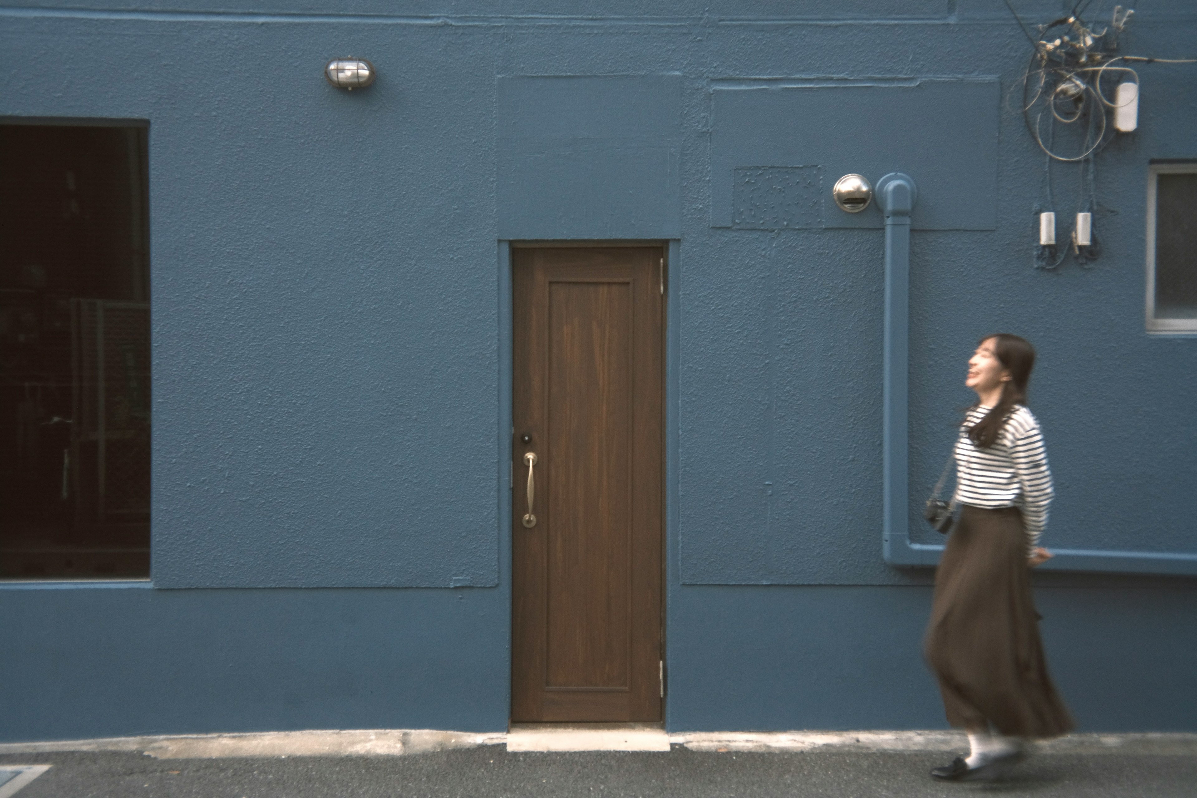 青い壁の前を歩く女性がいるシンプルな街の風景