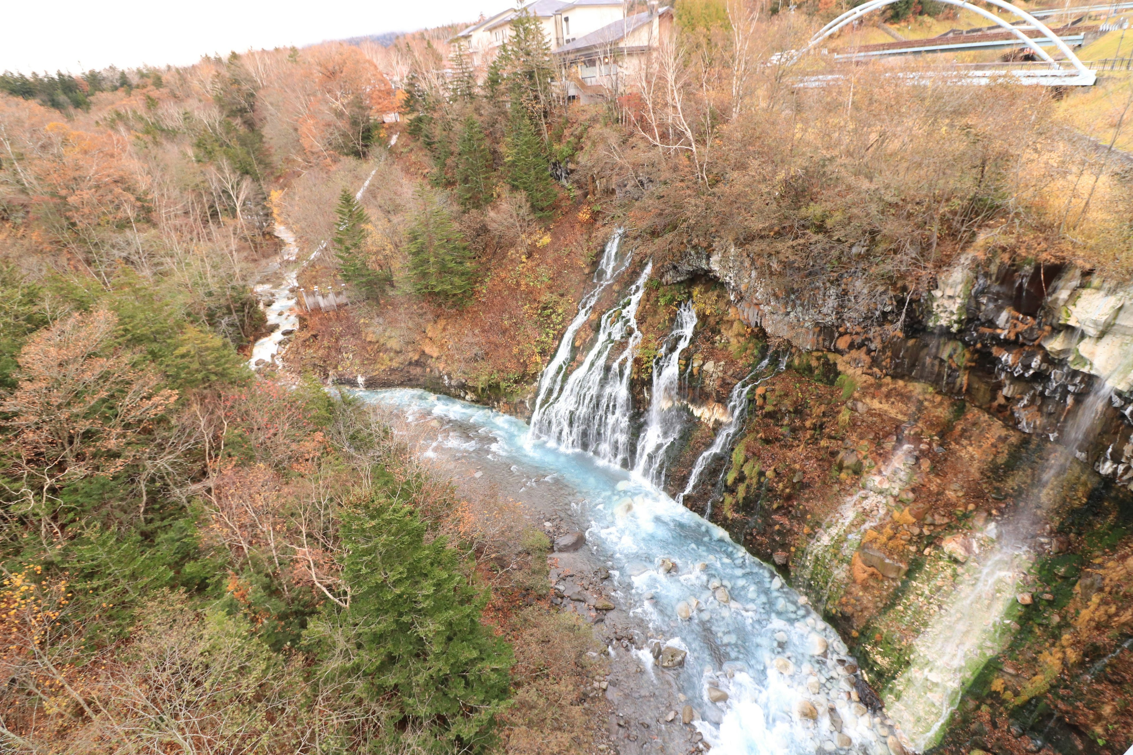 Cascata panoramica che scorre su scogliere rocciose circondate da foglie autunnali