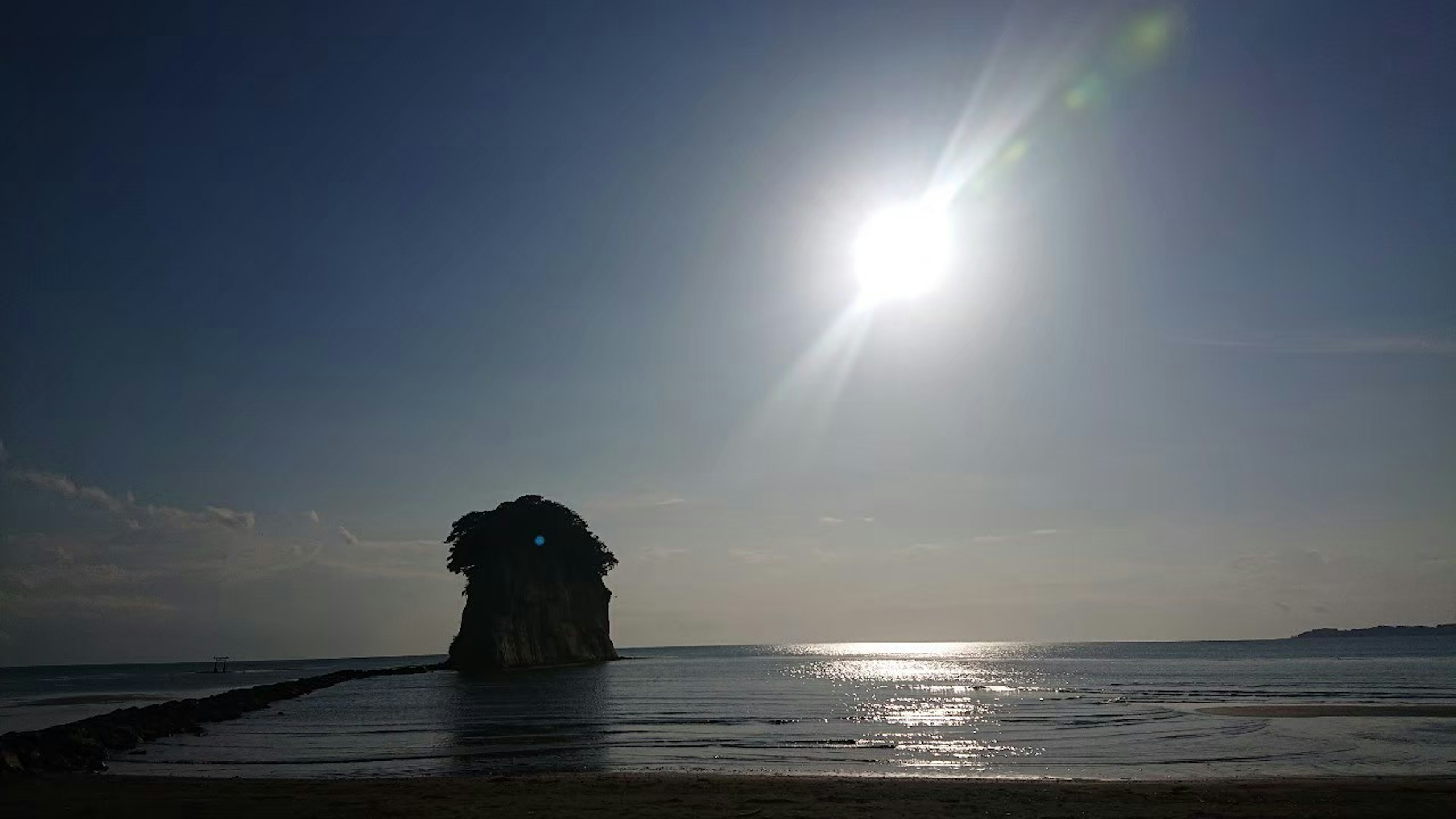 Escena costera con una gran formación rocosa y un sol brillante