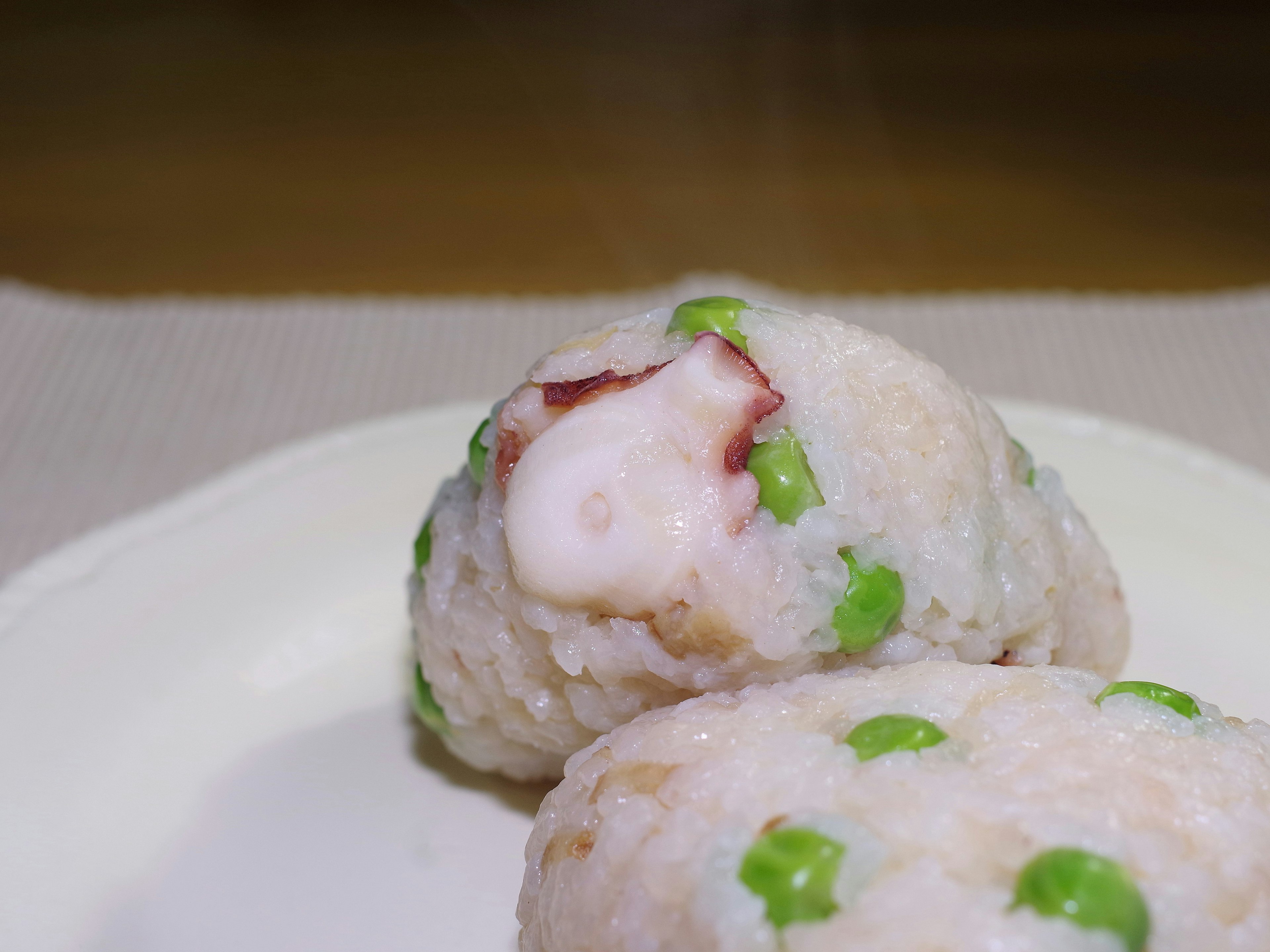 Sushi gurita dengan hiasan kacang polong hijau di atas piring putih