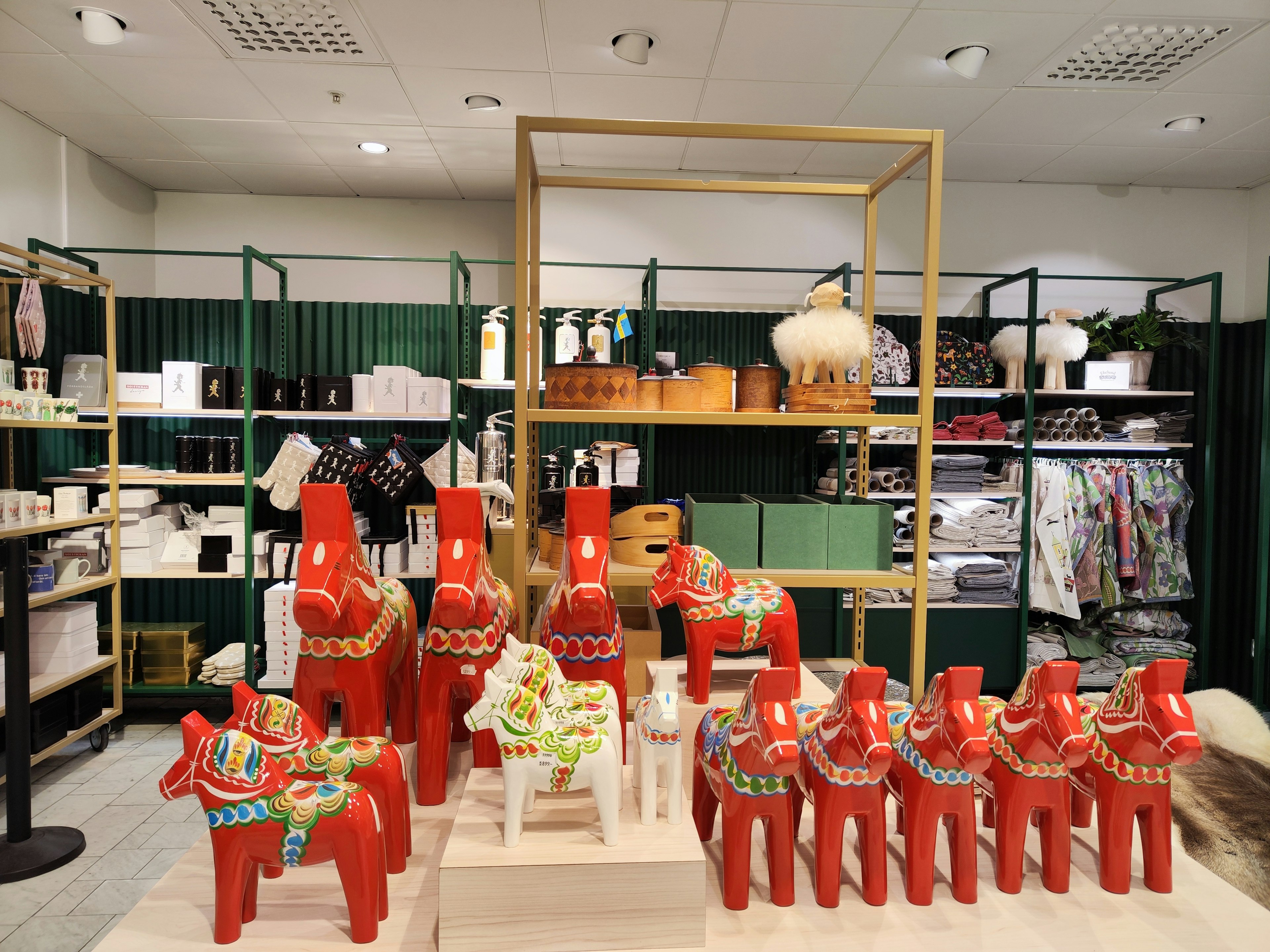 Display of red wooden horse figurines in a shop with various products and green backdrop