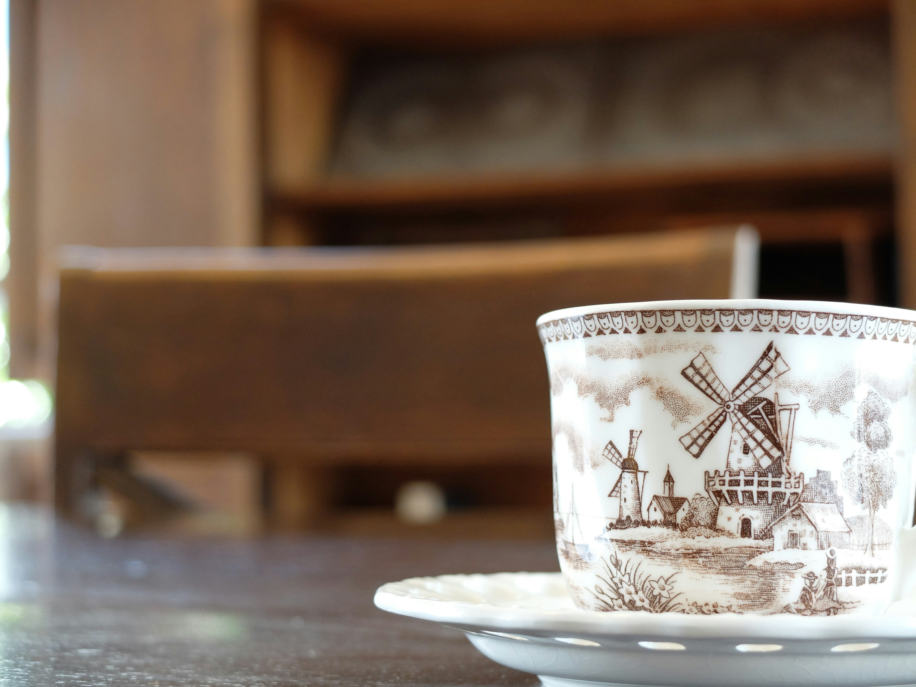 A cup with a windmill design placed on a saucer on a wooden table