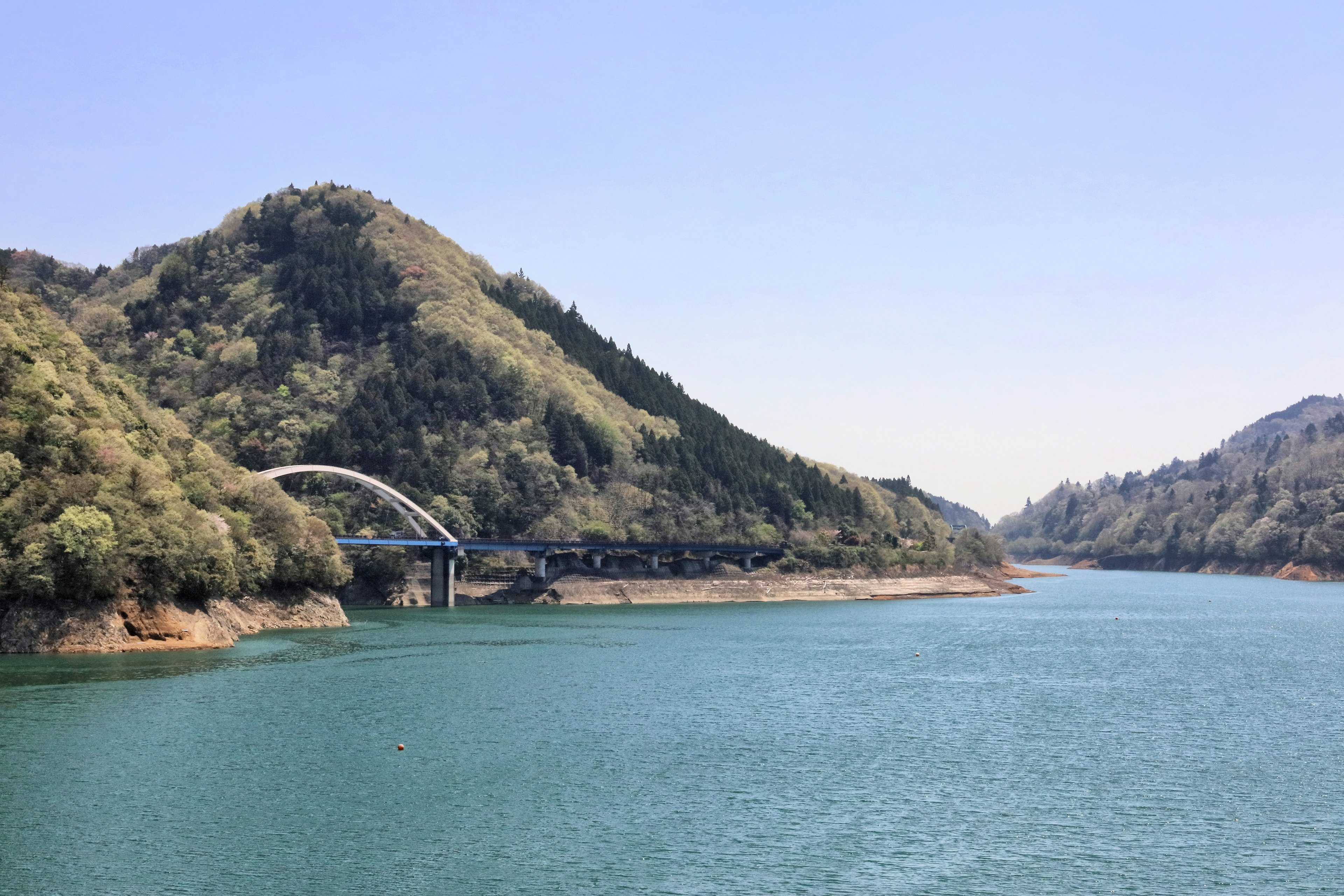 Vue panoramique d'un lac bleu entouré de collines vertes avec un pont en travers