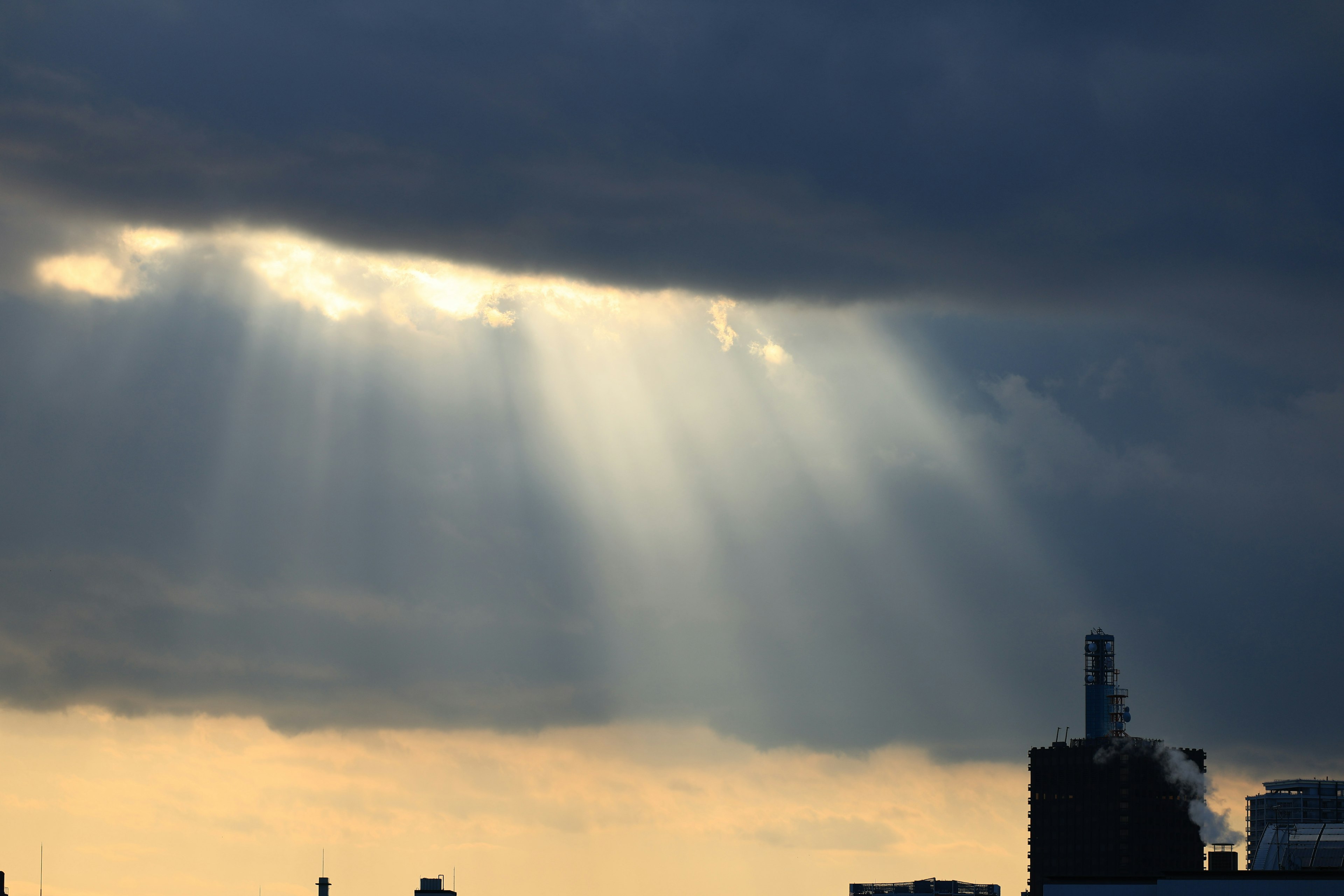 Lichtstrahlen, die durch dunkle Wolken scheinen, mit der Silhouette einer Fabrik