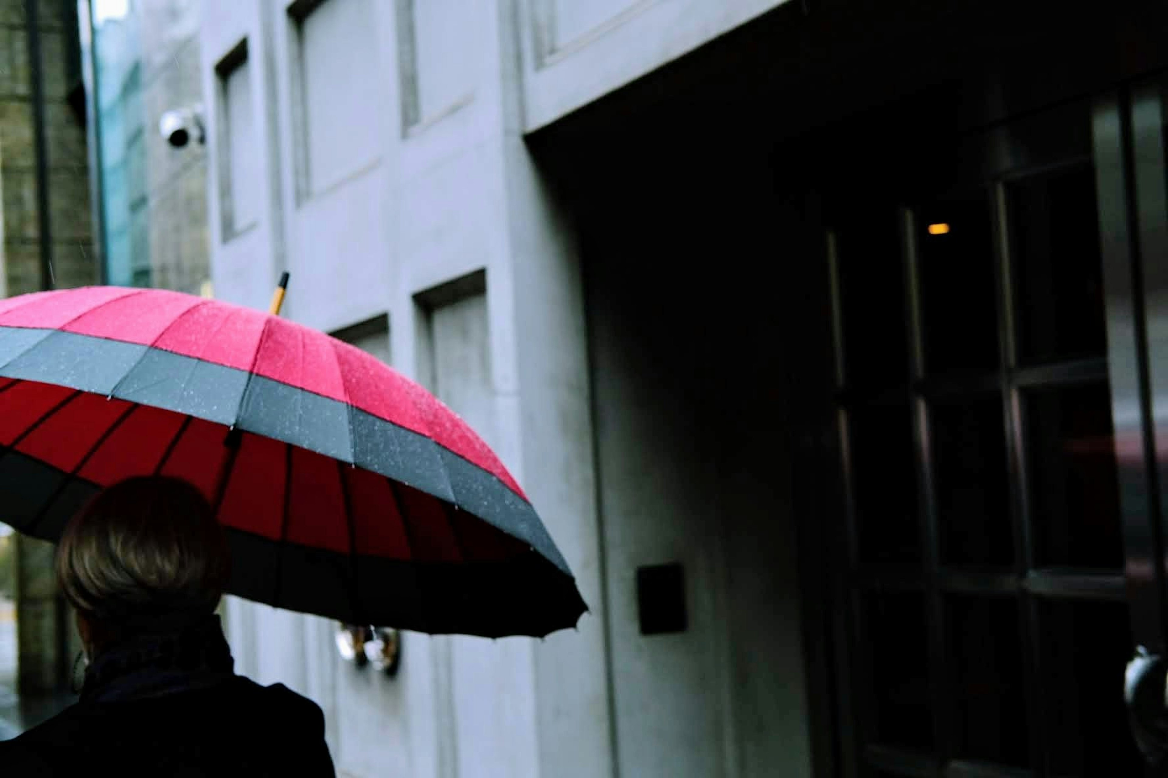 Person walking with a red and gray umbrella in front of a building