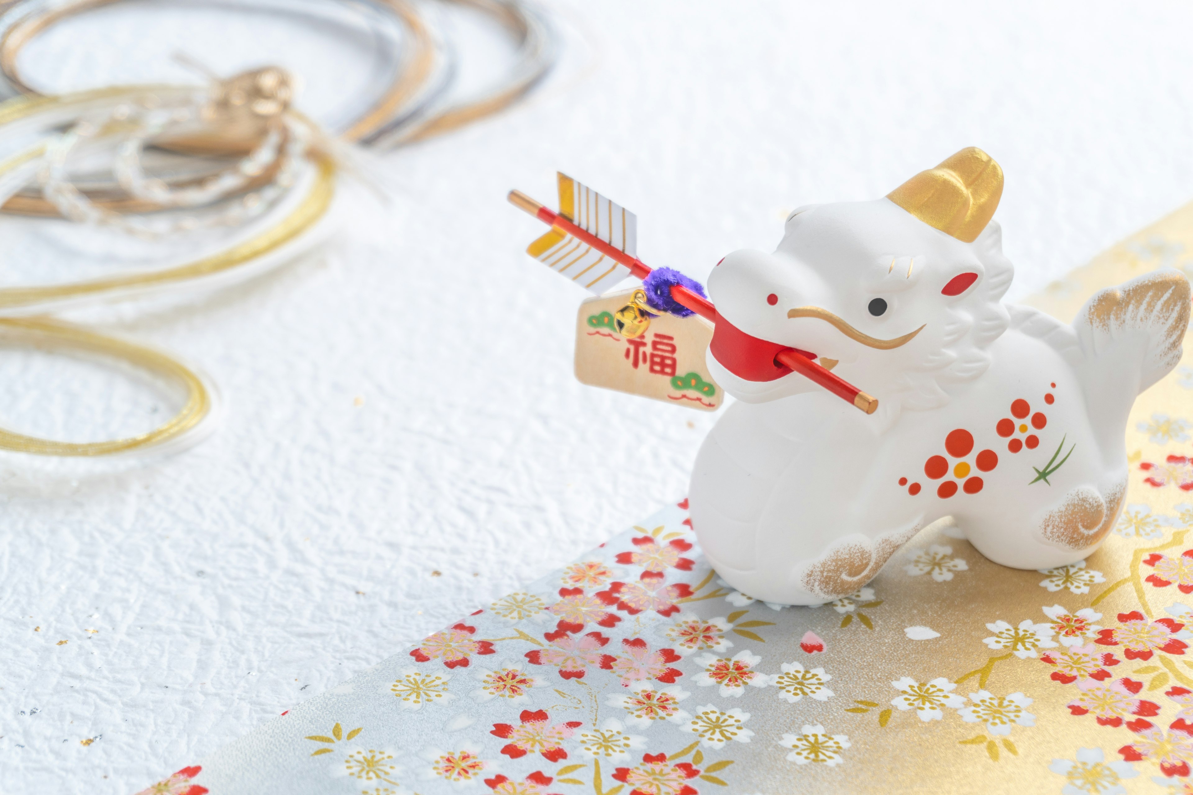 A white komainu figurine holding a red arrow with a blessing tag in its mouth