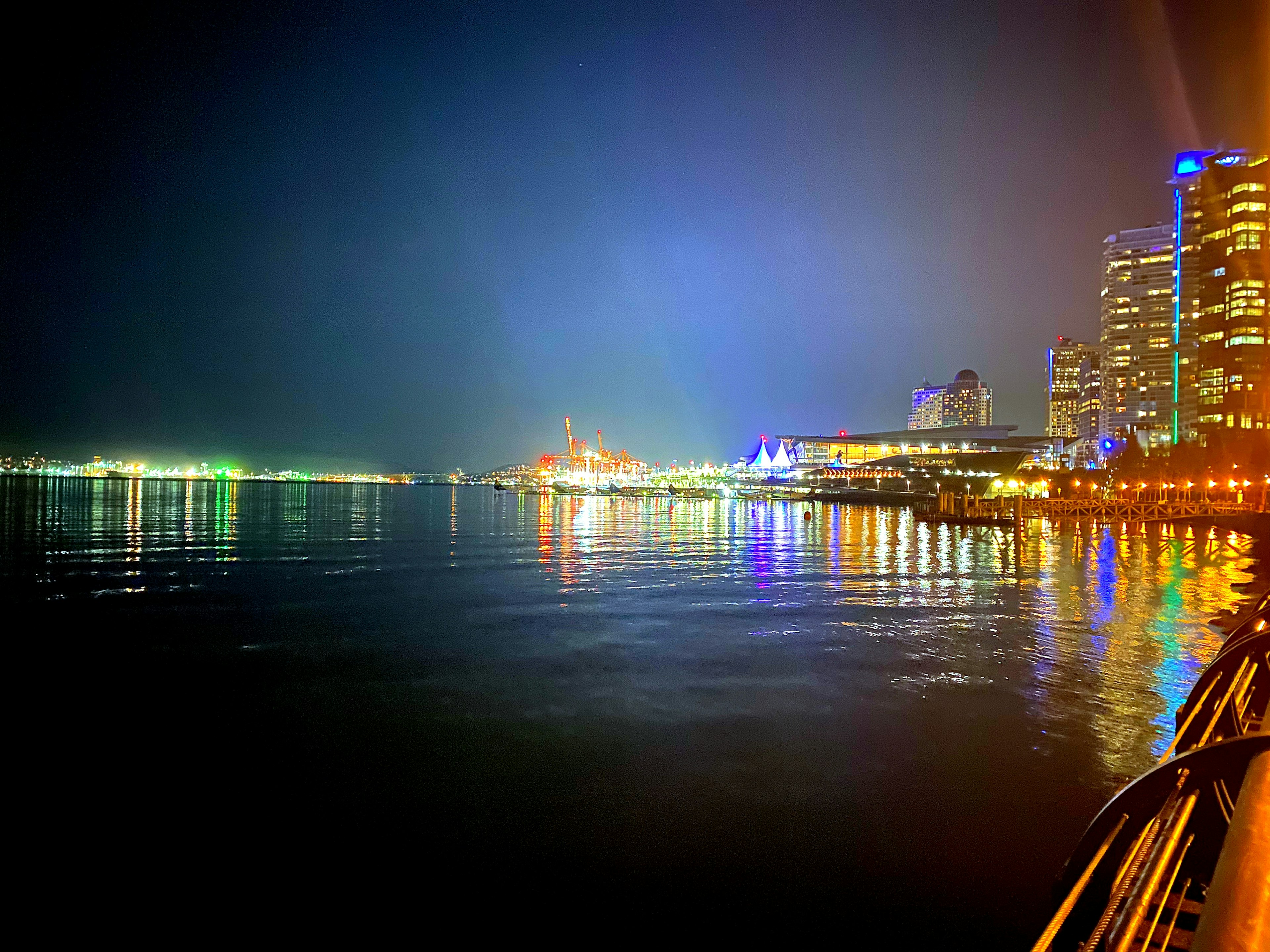 Vista nocturna de una ciudad costera con edificios iluminados y agua tranquila