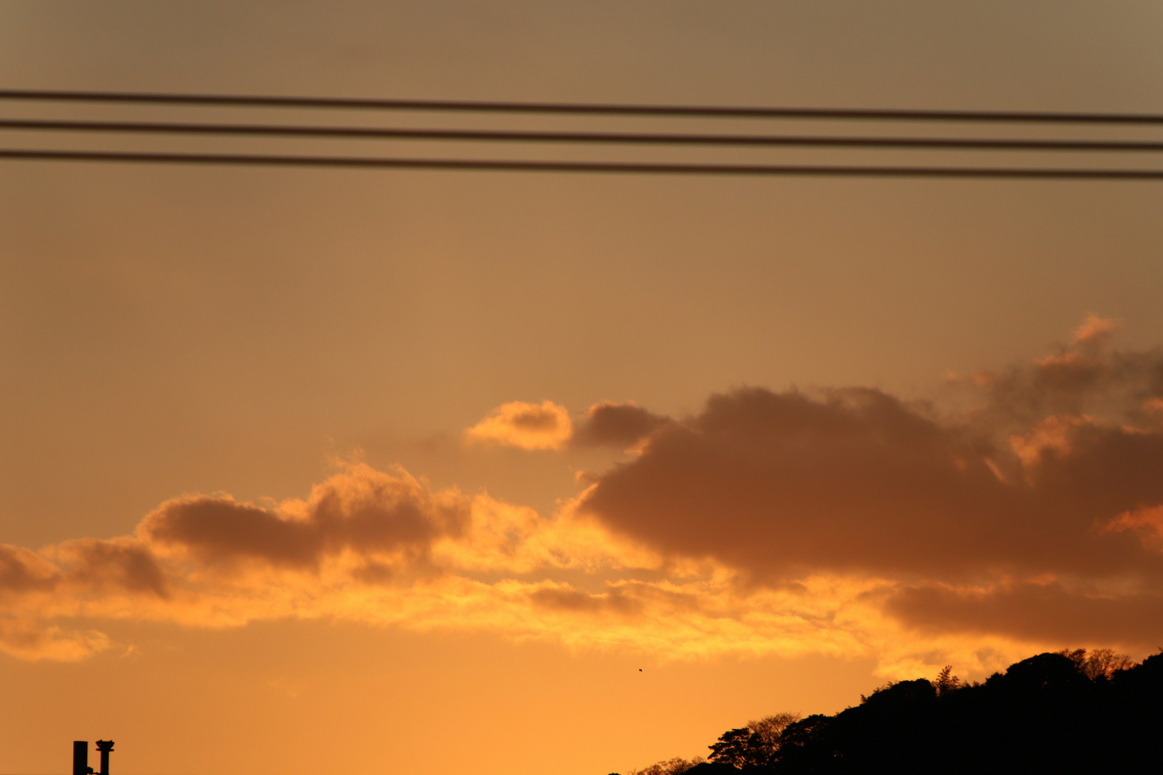 Oranger Sonnenuntergang mit Wolken und Stromleitungen